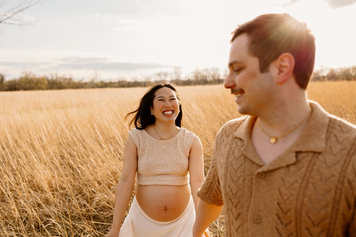 Two people share a joyful moment together in a sun-lit field of tall golden grass.