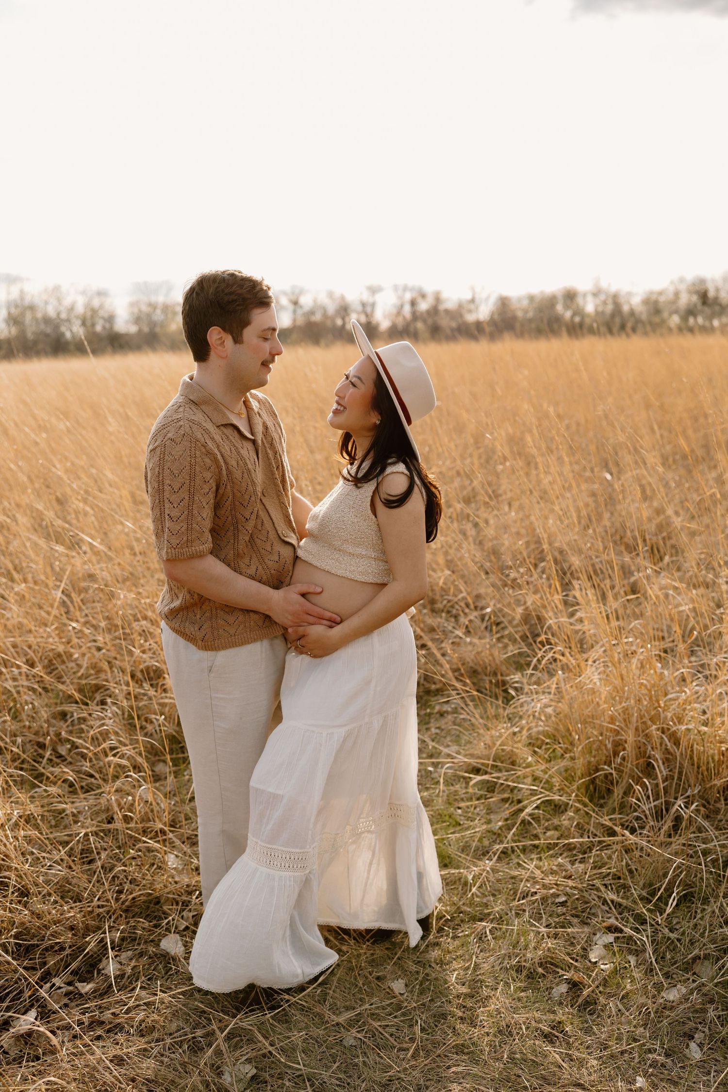 A couple poses intimately in a sun-lit field of tall golden grass.