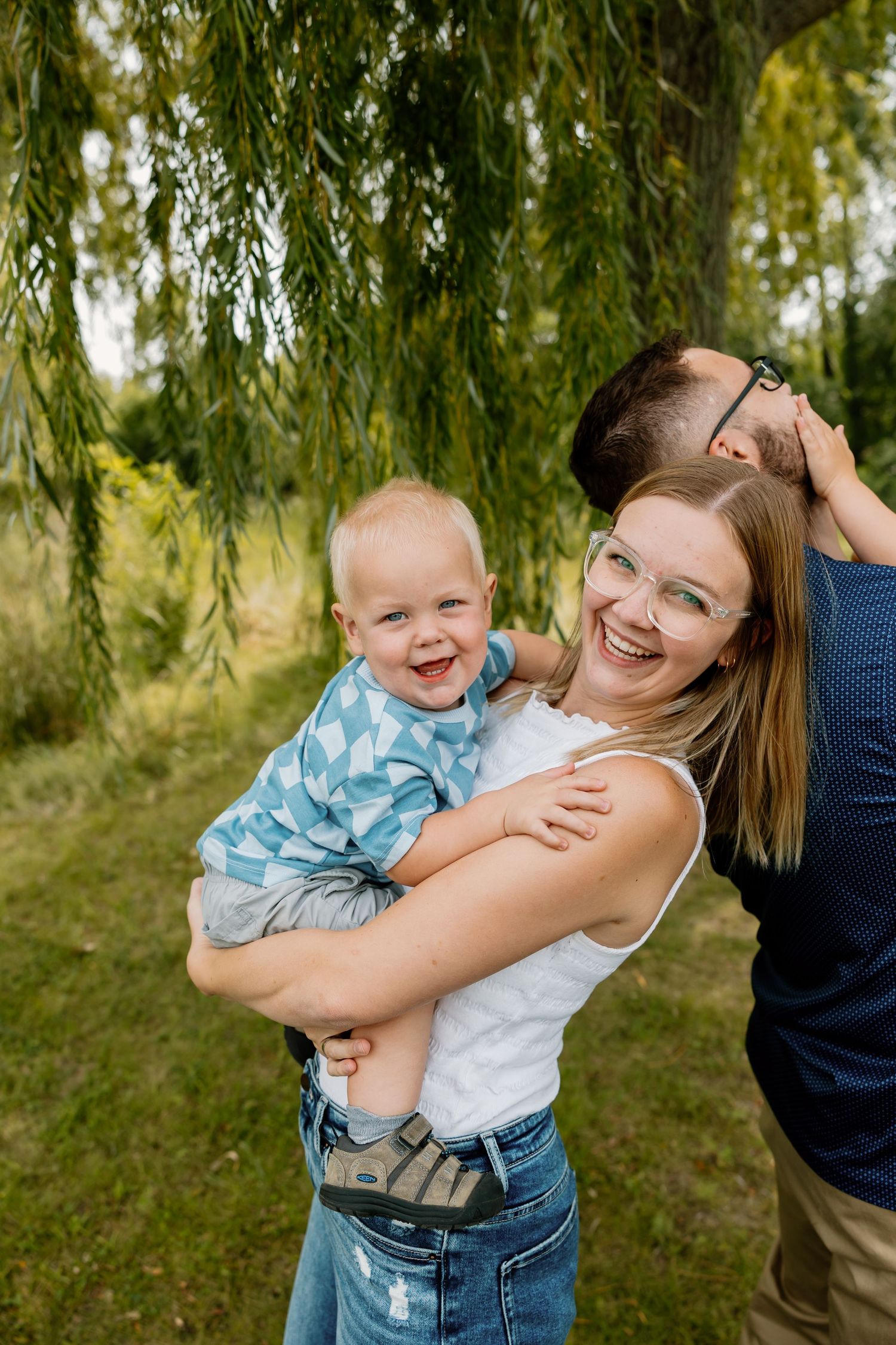 A joyful family moment captured under a weeping willow tree on a sunny day.