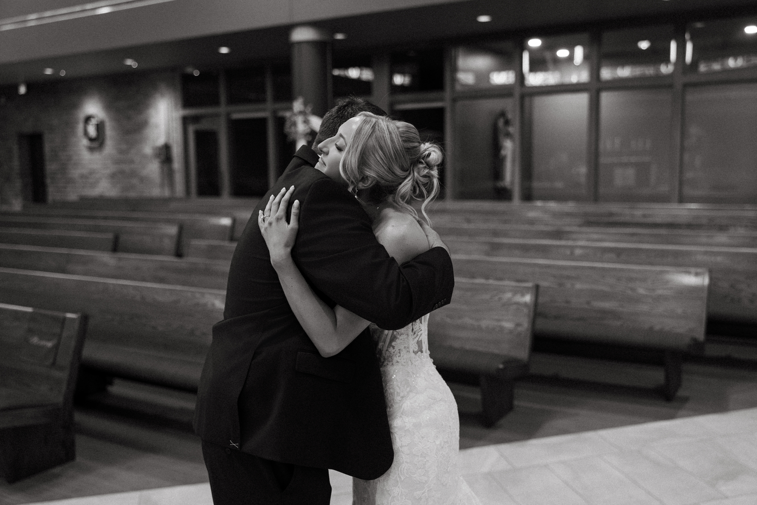 Black and white photo of a bride and groom sharing an emotional hug inside a church on their wedding day.