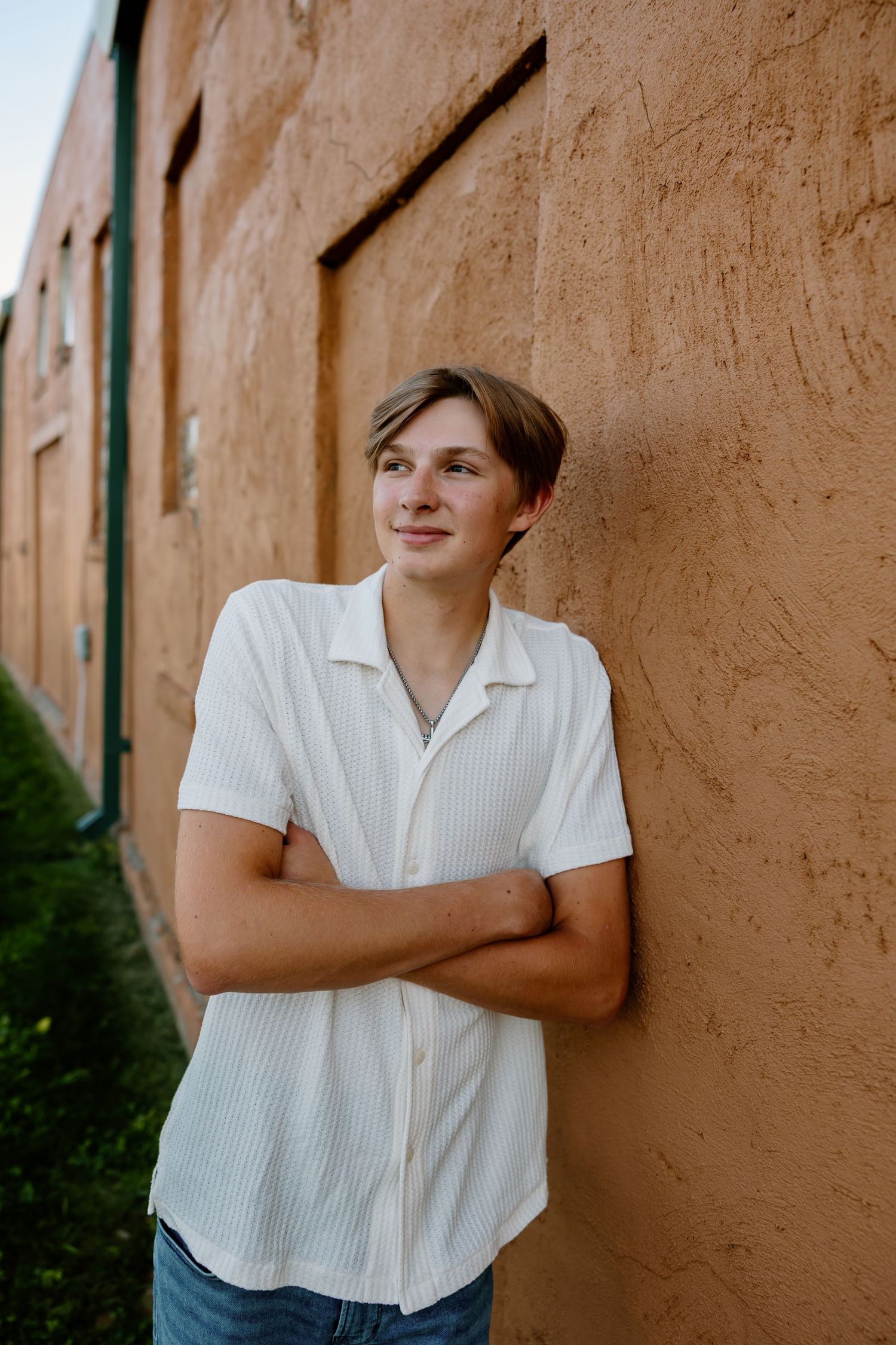 Someone wearing a white button-down shirt poses casually against a stucco wall outdoors.