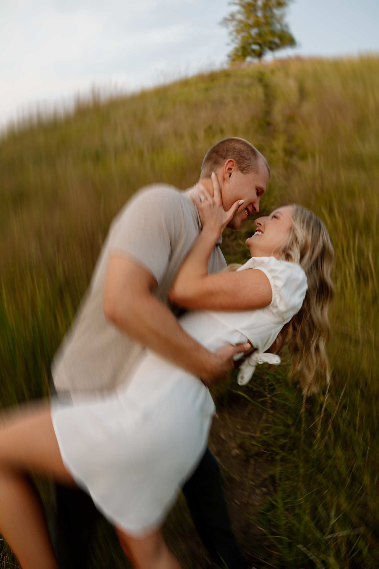 Romantic embrace on a hilltop surrounded by tall grass and golden sunlight.