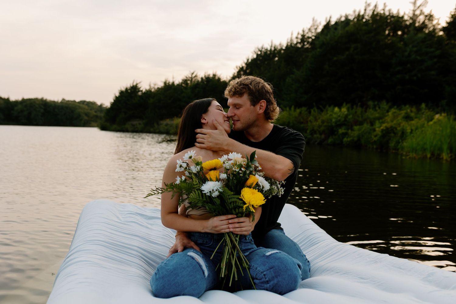 Romantic couple sits on mattress by lake with wildflower bouquet at sunset.
Sioux Falls Photographer  
Evermore Photo Co