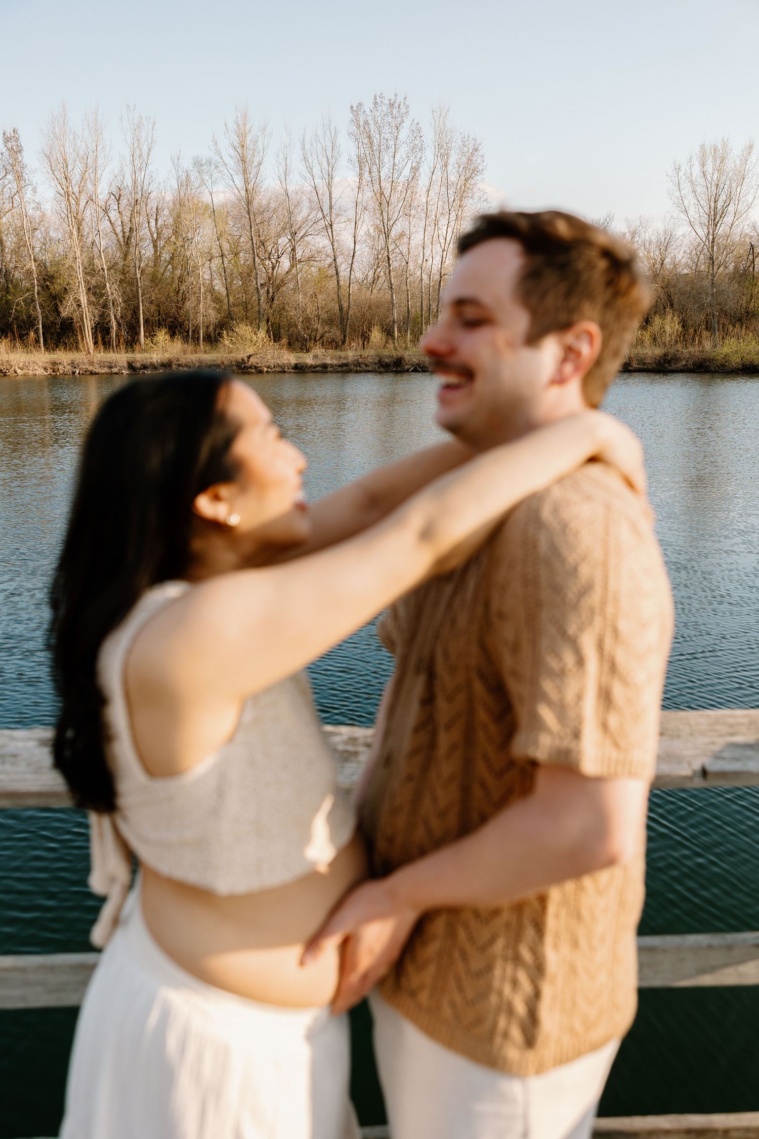 A romantic couple embraces on a wooden dock by a serene lake during golden hour.
