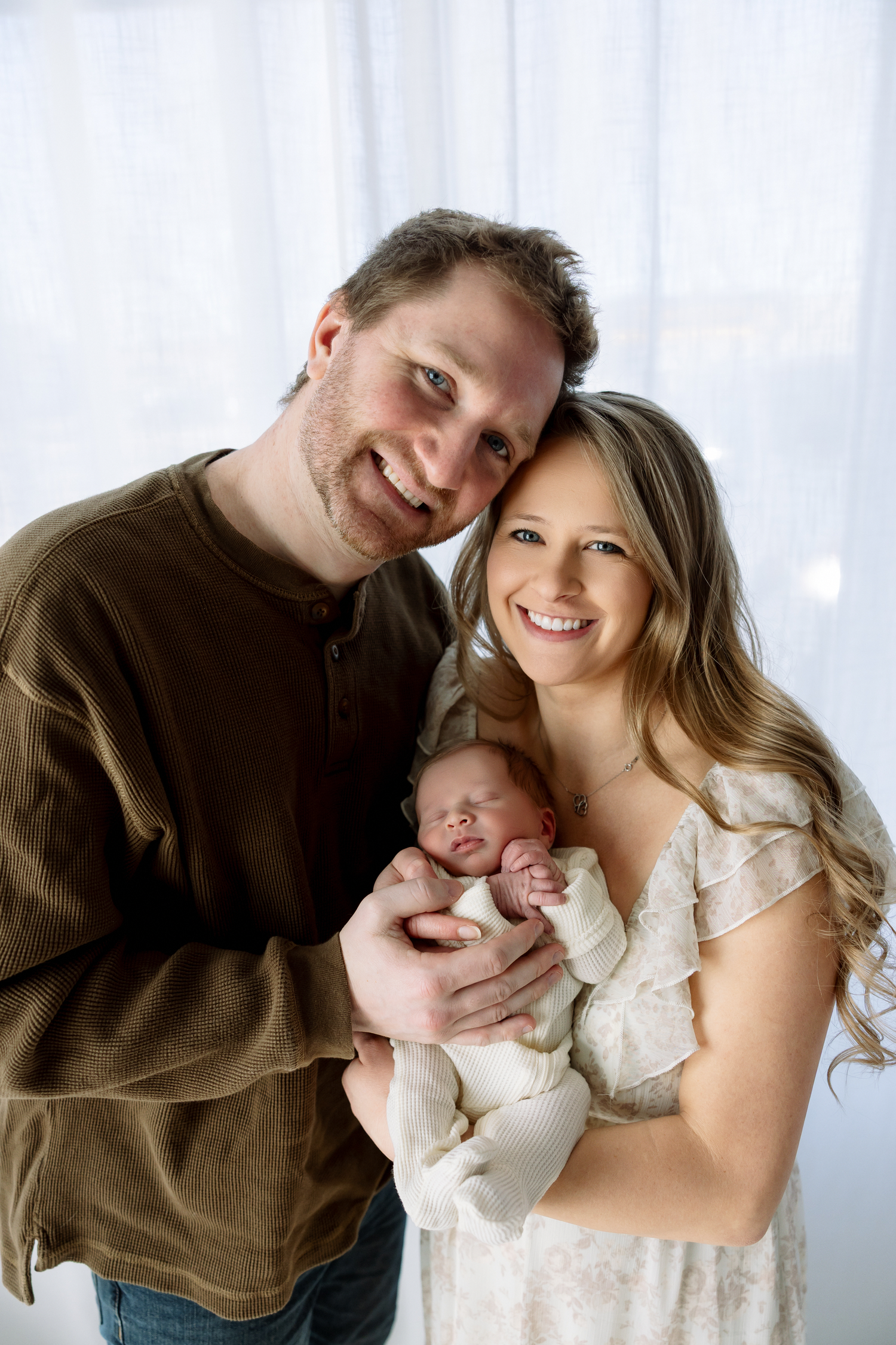 A happy couple embraces their newborn baby in a series of tender portrait photographs against a light background.