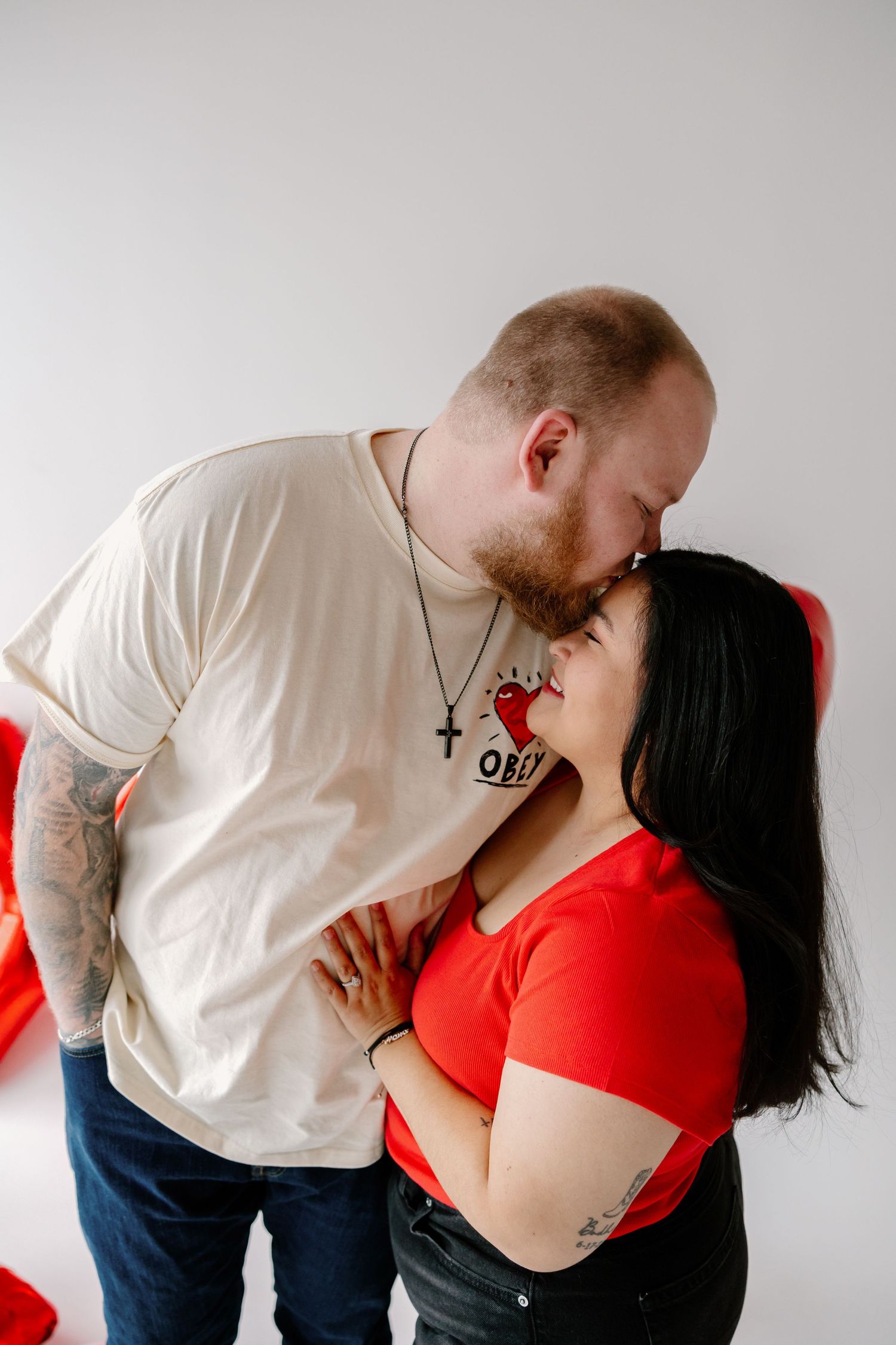 A couple in red and white t-shirts share an intimate moment against a white wall.