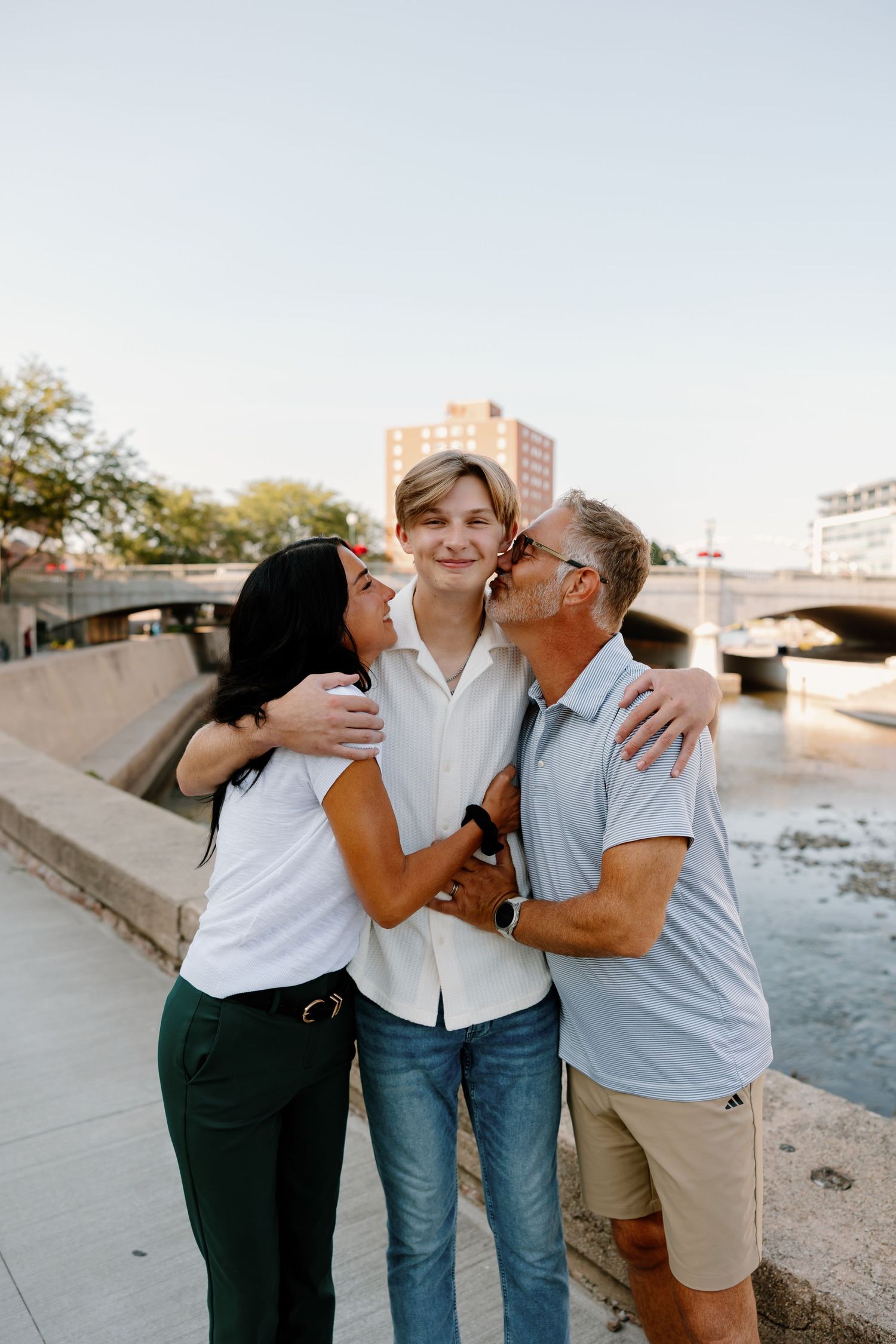 Family of three sharing affectionate moments together at sunset by a waterfront.