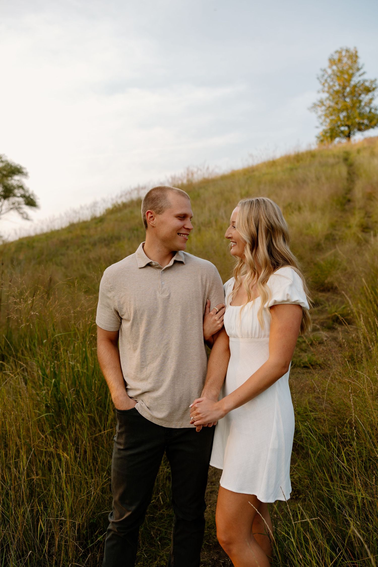 A romantic couple enjoying a sunset moment together on a grassy hillside wearing casual attire.