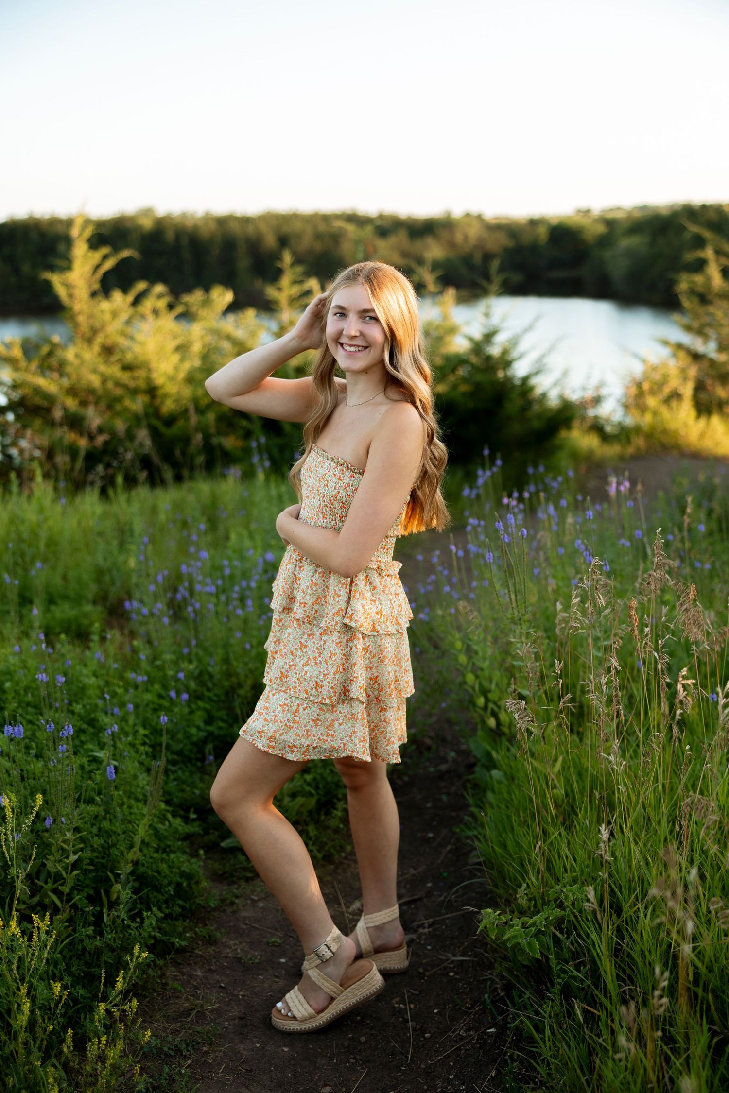 A joyful outdoor portrait featuring a sundress amidst wildflowers with a lake in the background.