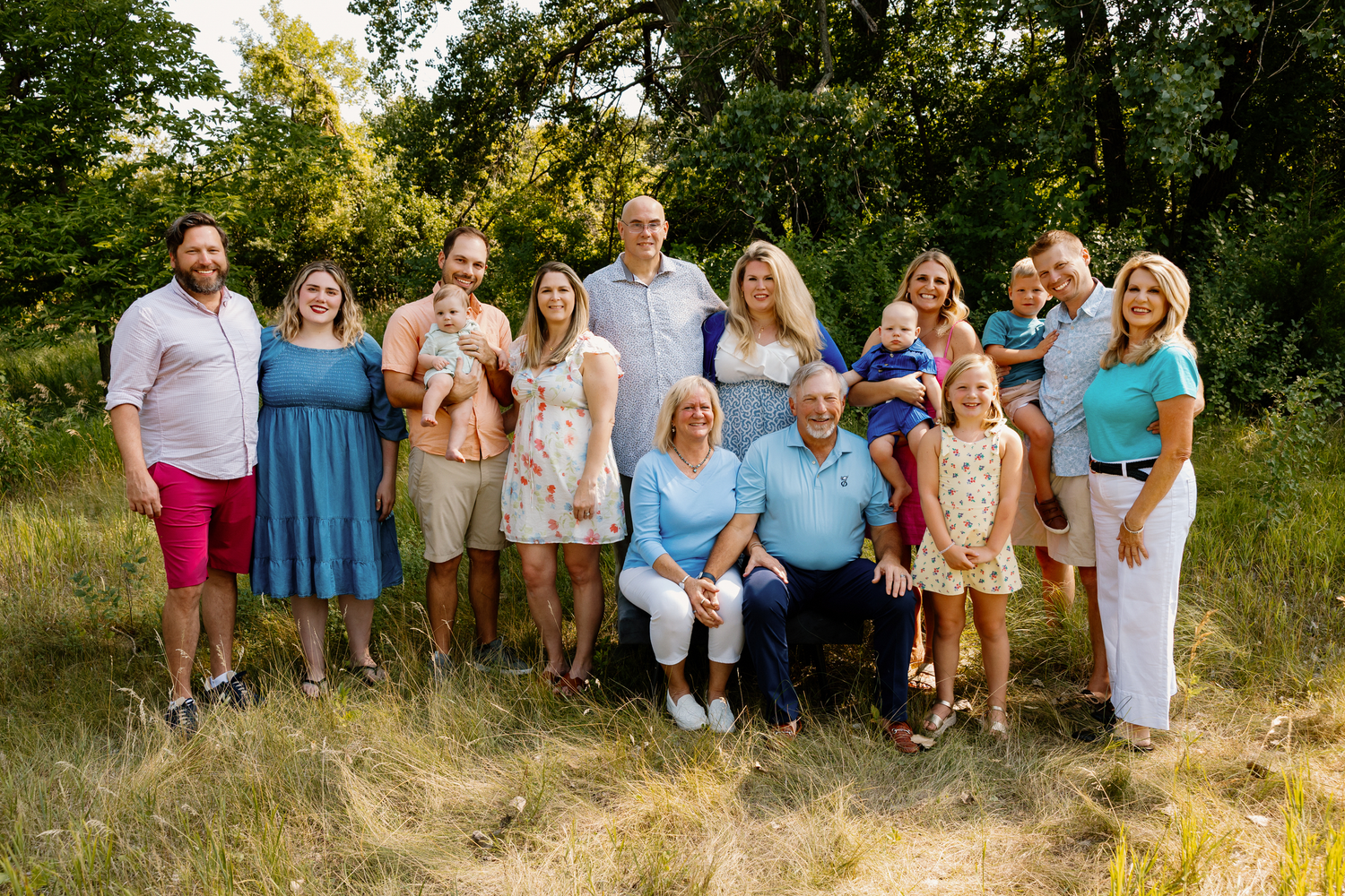 Large family group portrait outdoors in a lush green meadow, smiling together for a summer family photo session.