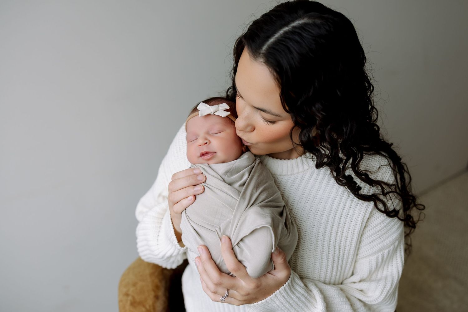 A tender family moment captured in soft, neutral tones as parent and baby share an intimate embrace.