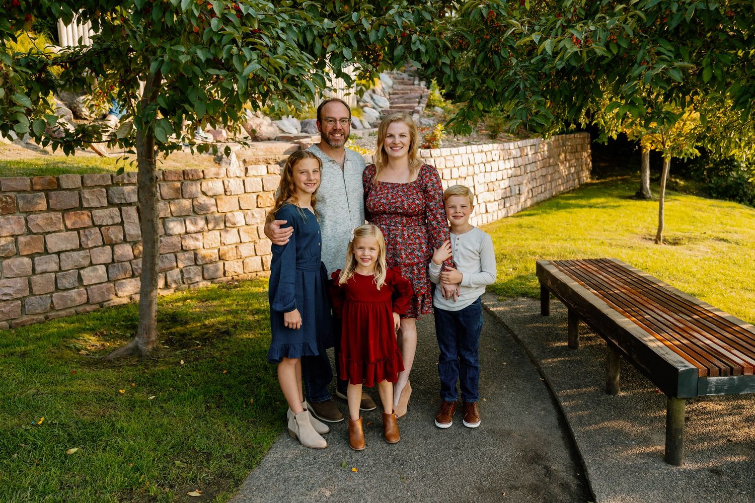 A group poses for outdoor family photos in a garden setting with stone walls and benches in the background.