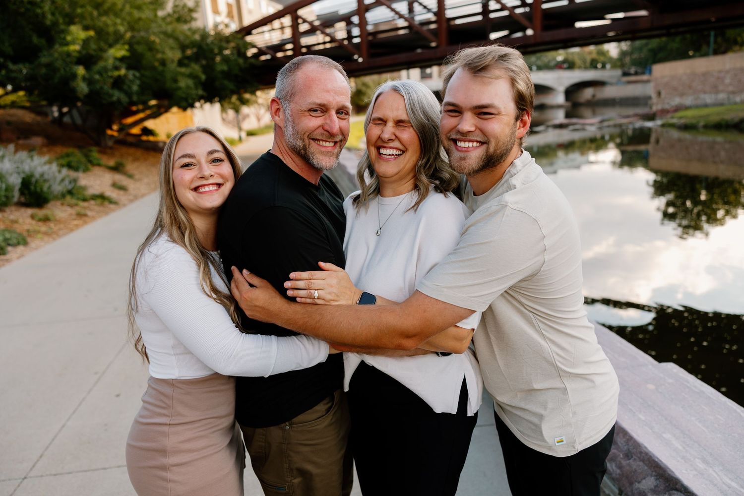 A group of people embrace and laugh together while wearing casual white and black outfits outdoors.