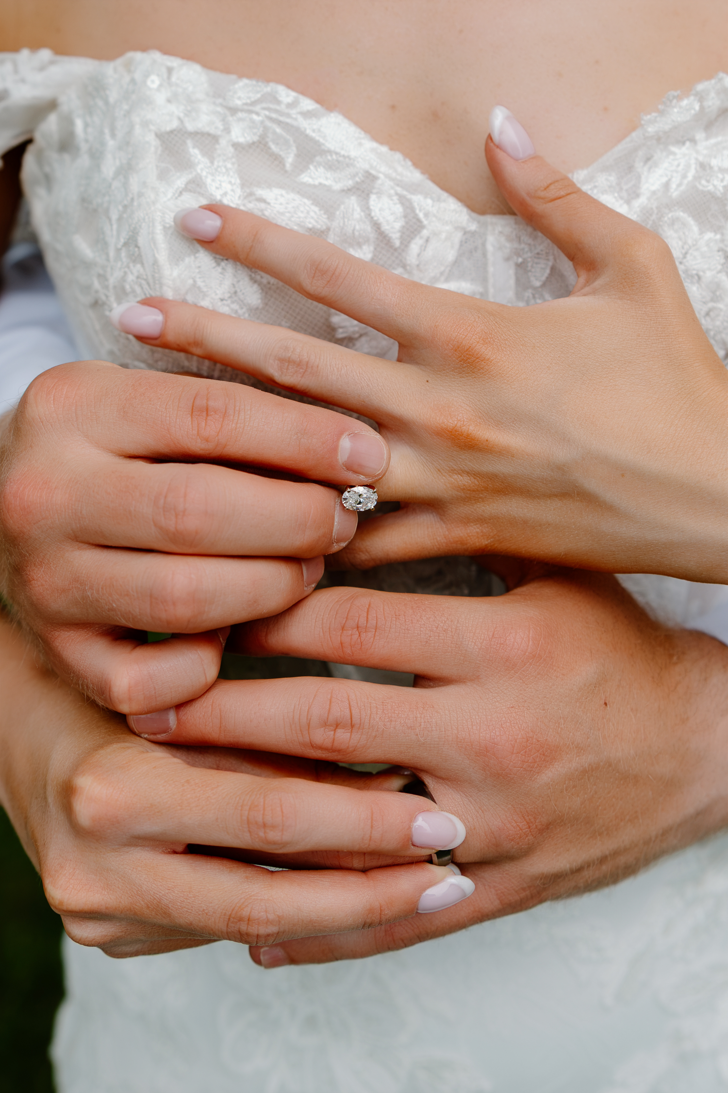 Close-up of bride and groom hands embracing, showcasing a sparkling diamond engagement ring on her finger.