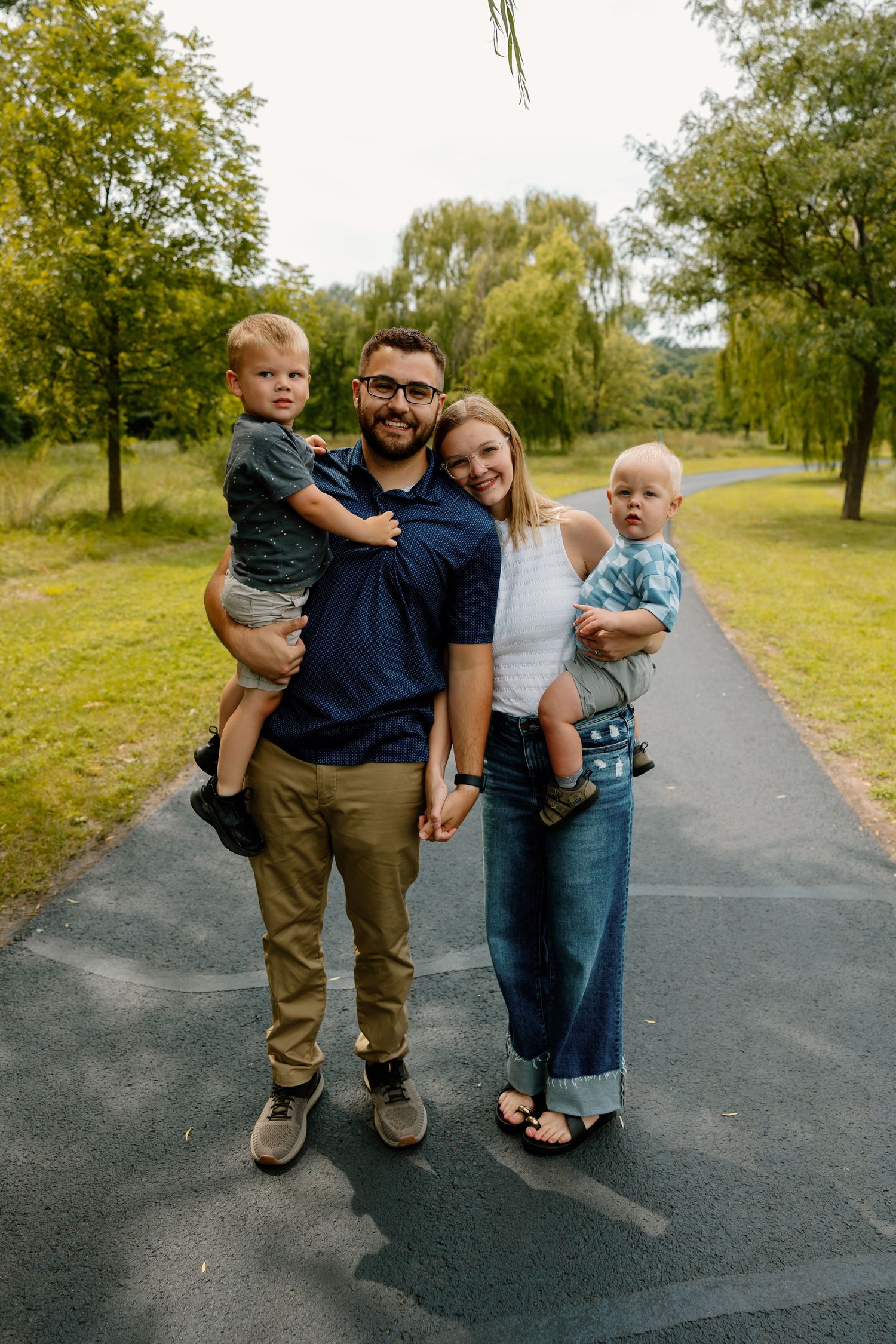 A family poses joyfully together on a tree-lined path on an autumn day.