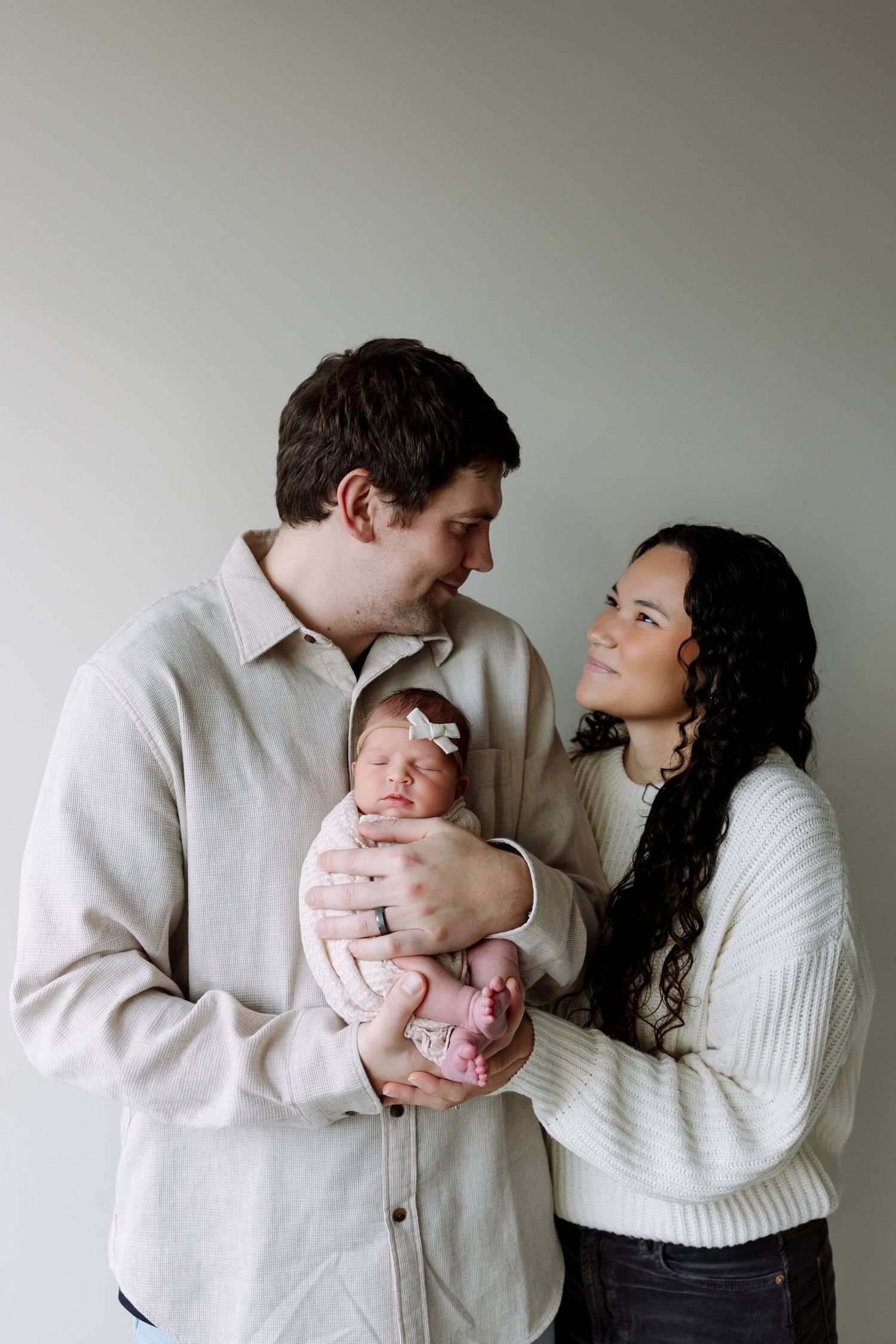 A couple in white sweaters share tender moments with their newborn baby in a series of intimate family portraits.
