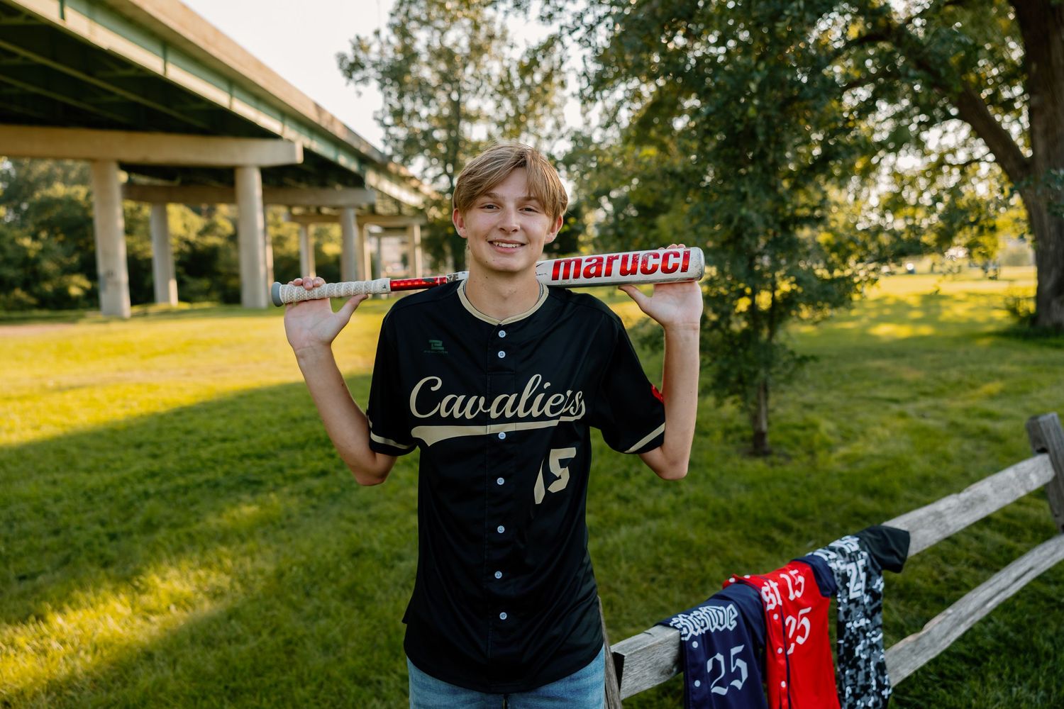 Student athlete poses outdoors near baseball field equipment during golden hour sunset photoshoot.