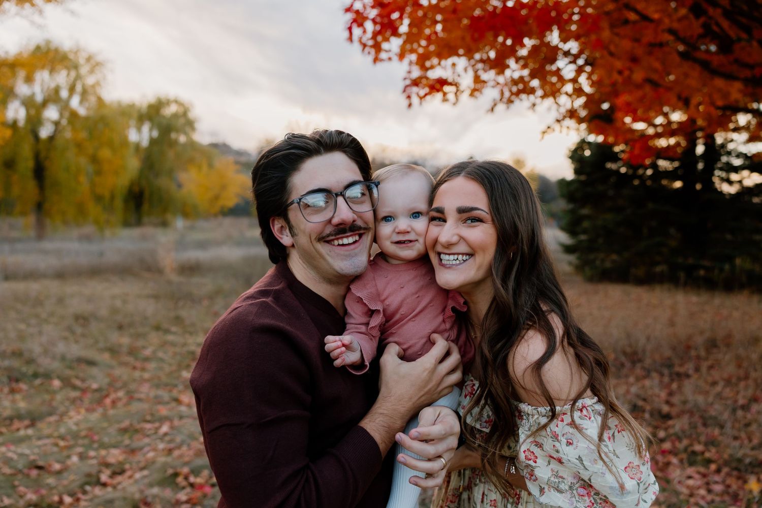A couple shares joyful moments together in a scenic autumn setting with colorful fall foliage in the background.