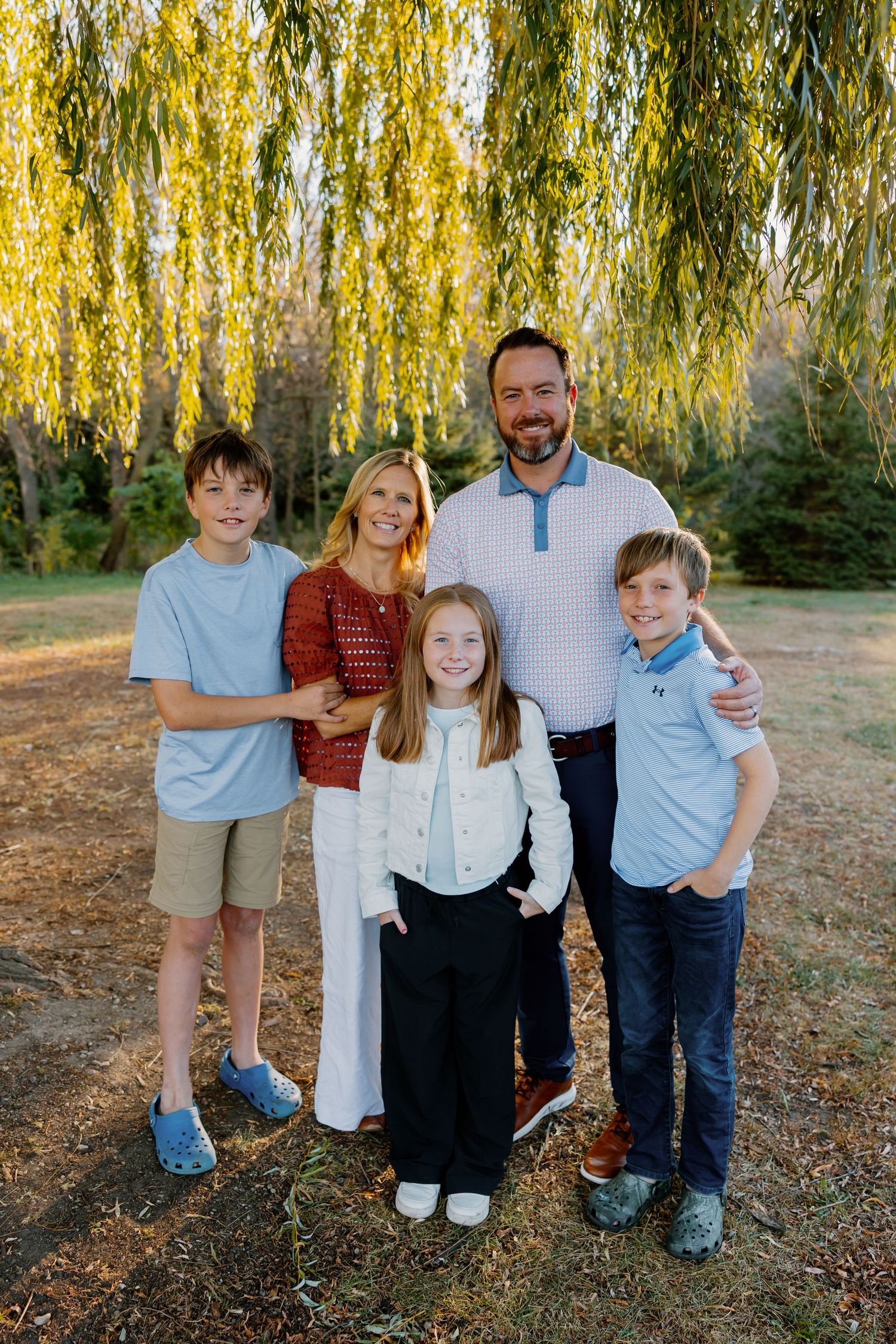 A family poses together under a golden willow tree on an autumn afternoon.