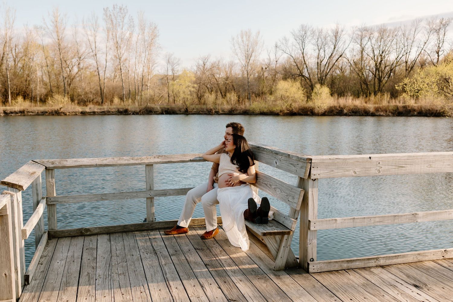A person sits on a wooden dock overlooking a serene lake on an autumn afternoon.