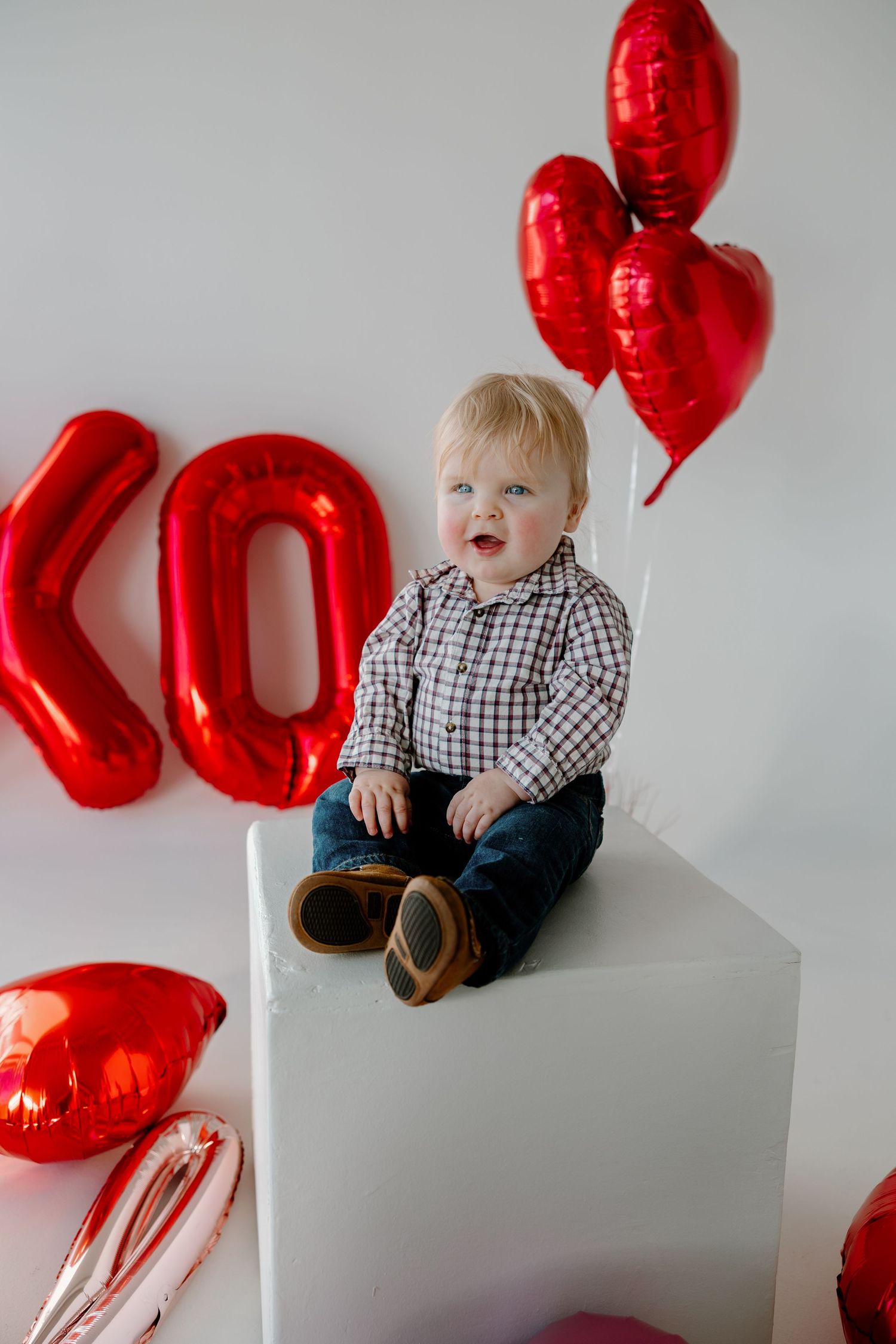 A festive Valentine's photo setup with red balloon letters and heart balloons against a white backdrop.