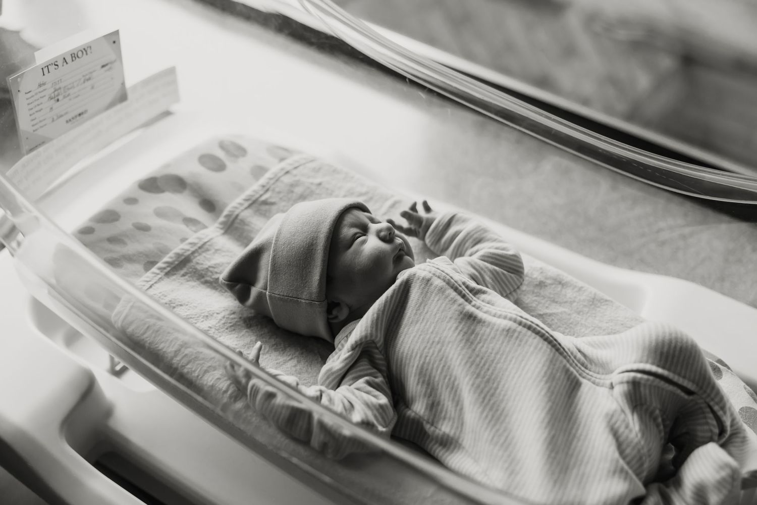 A serene black and white image of a newborn baby sleeping peacefully in a hospital bassinet.