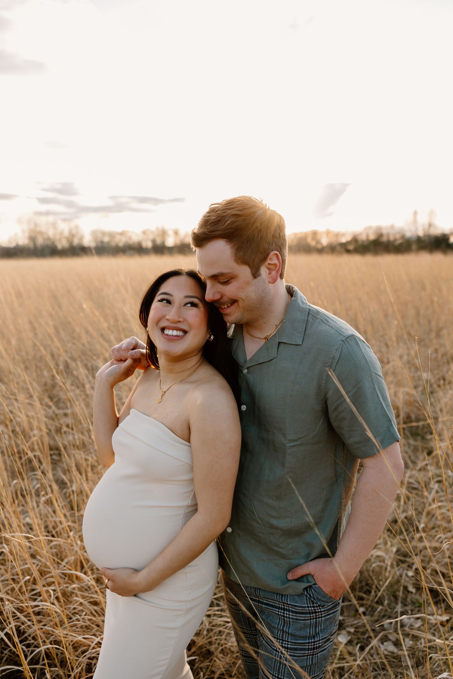 A maternity photo shoot in a sunlit field of tall grass during golden hour.