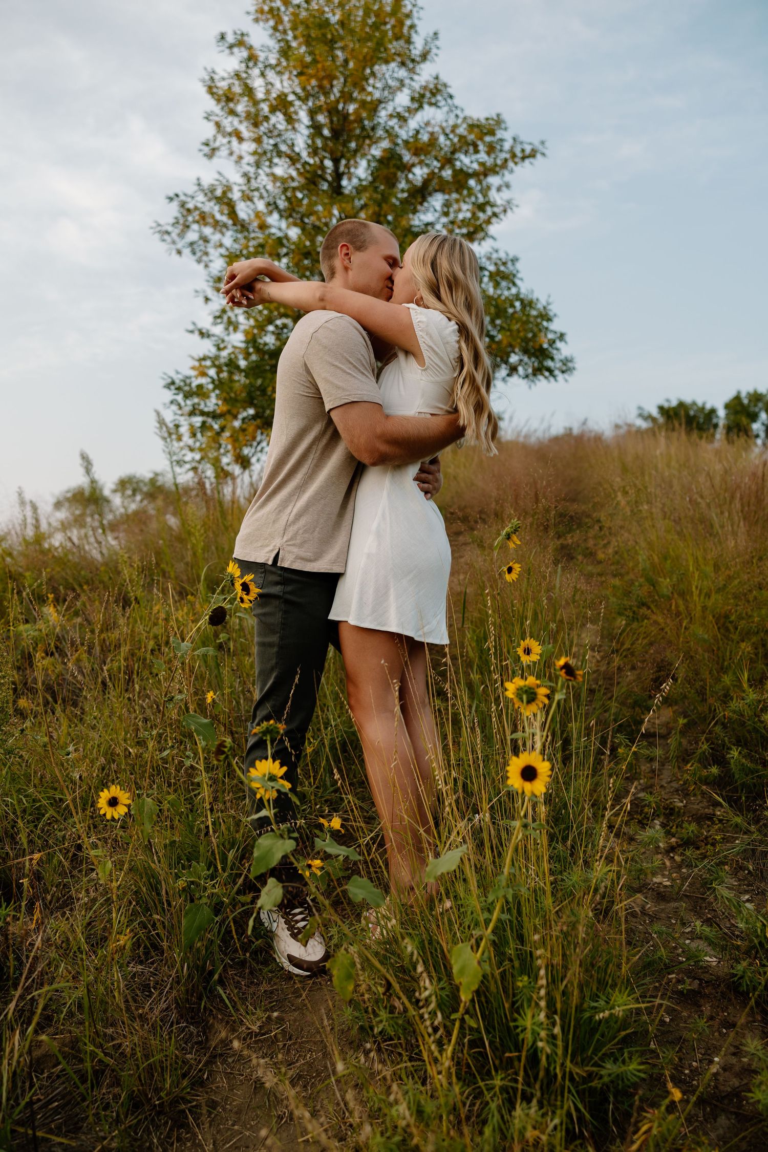 Playful couple dancing among wild sunflowers on a grassy hillside.