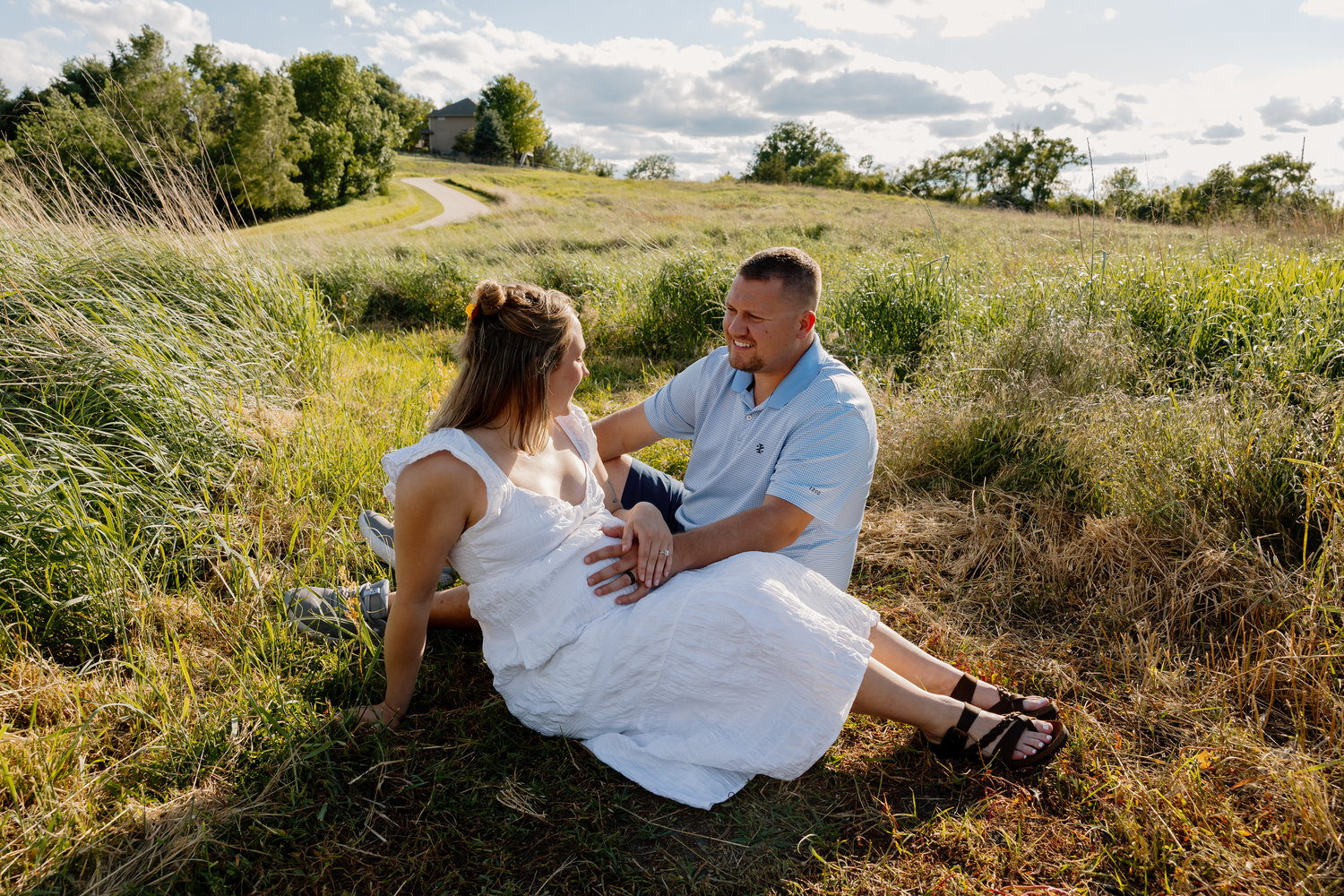 Couple sitting together in a lush green field, sharing a romantic moment on a sunny day.
