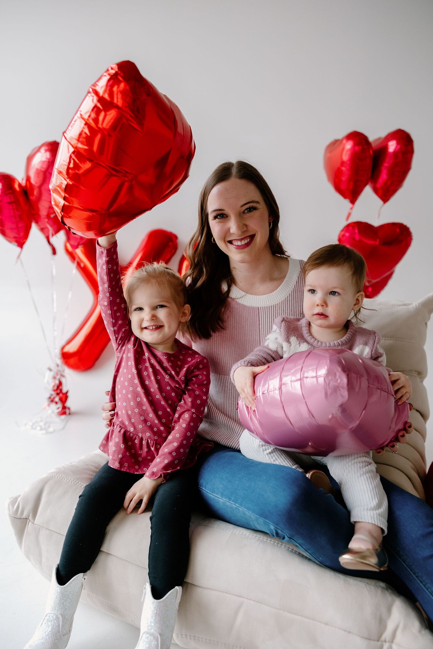 Three people sitting on a white couch with red heart-shaped balloons for Valentine's Day celebration.
