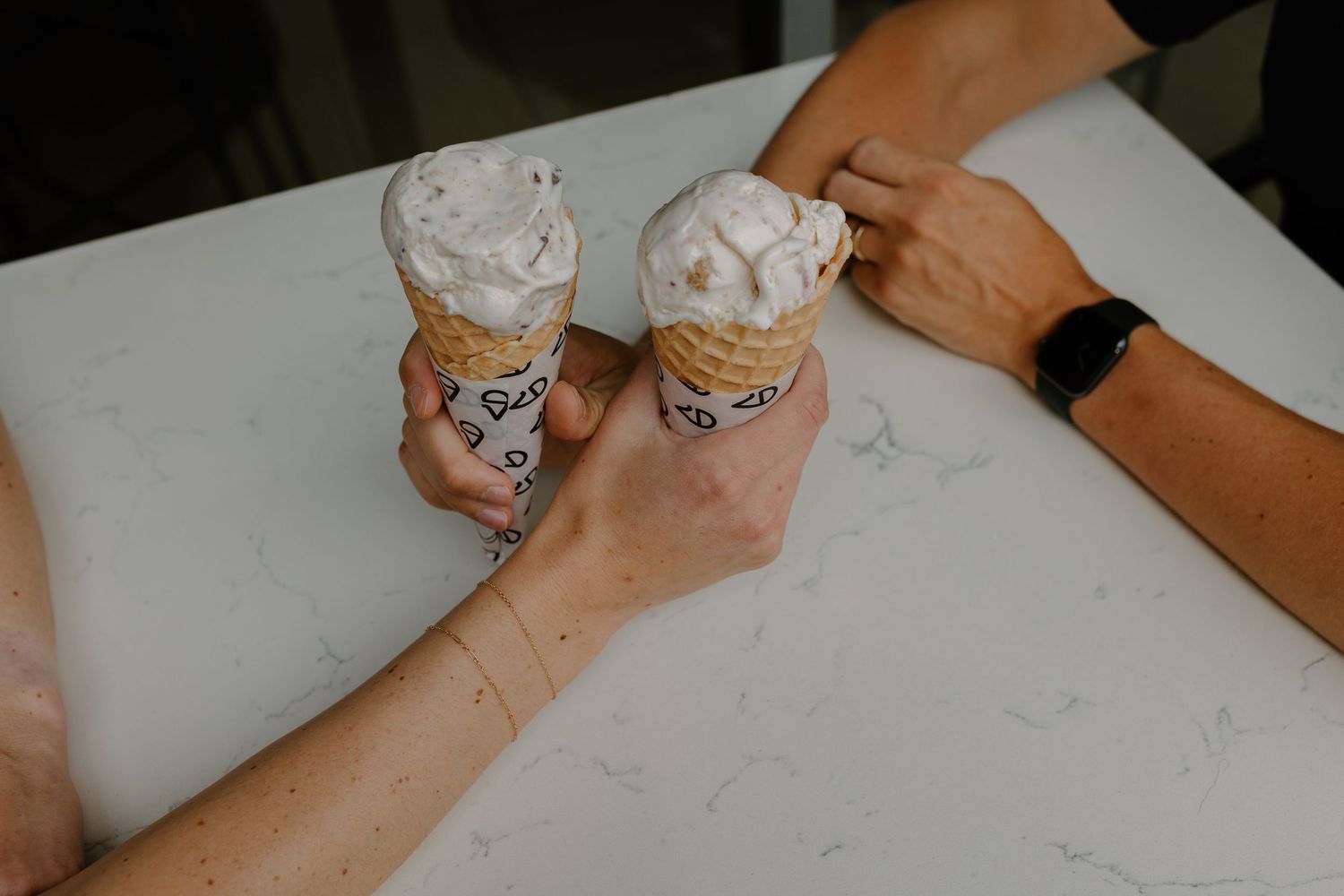 Two ice cream sundaes being shared on a white table surface.