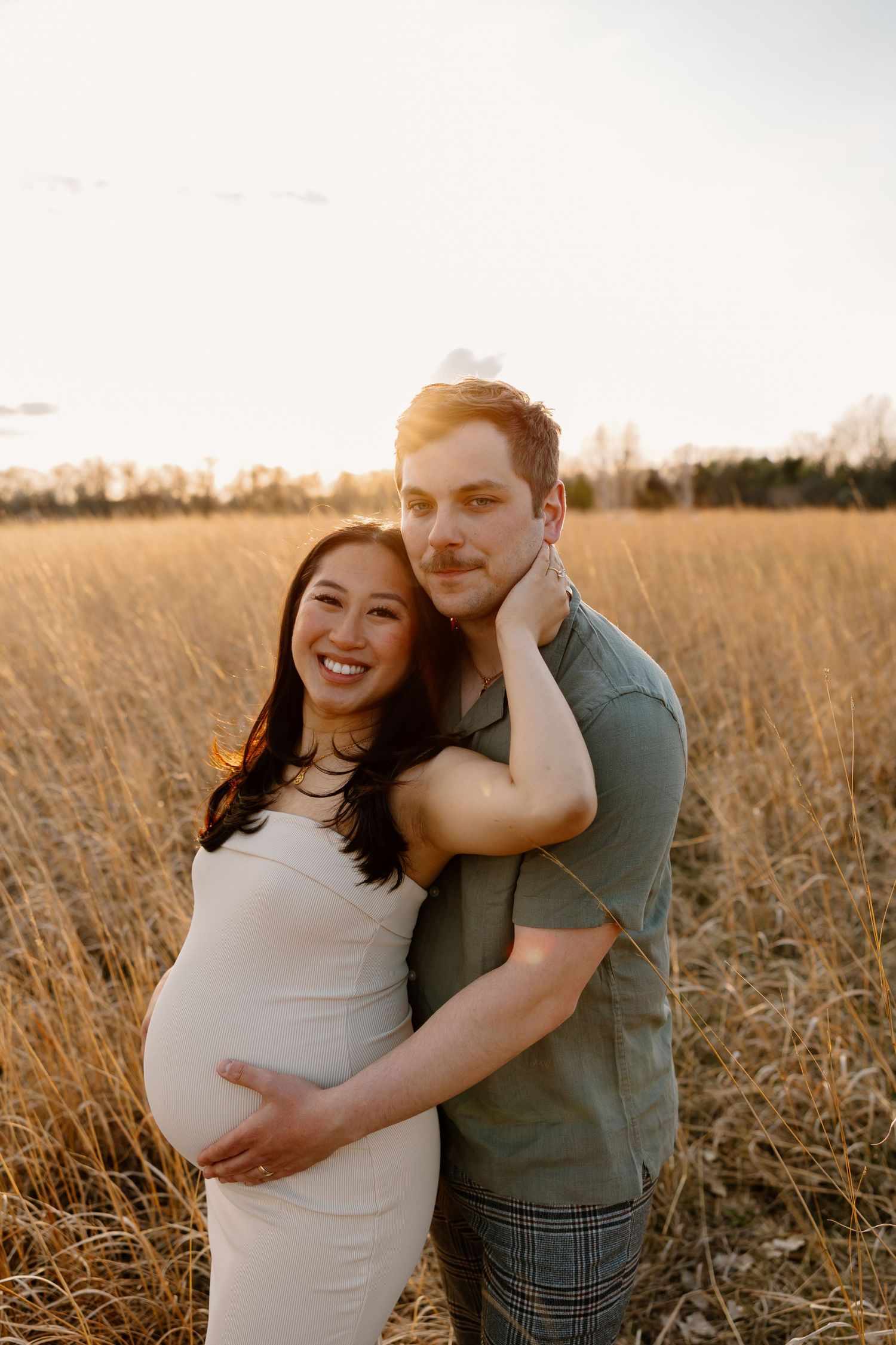 A sunset maternity portrait of a couple embracing in a golden wheat field.