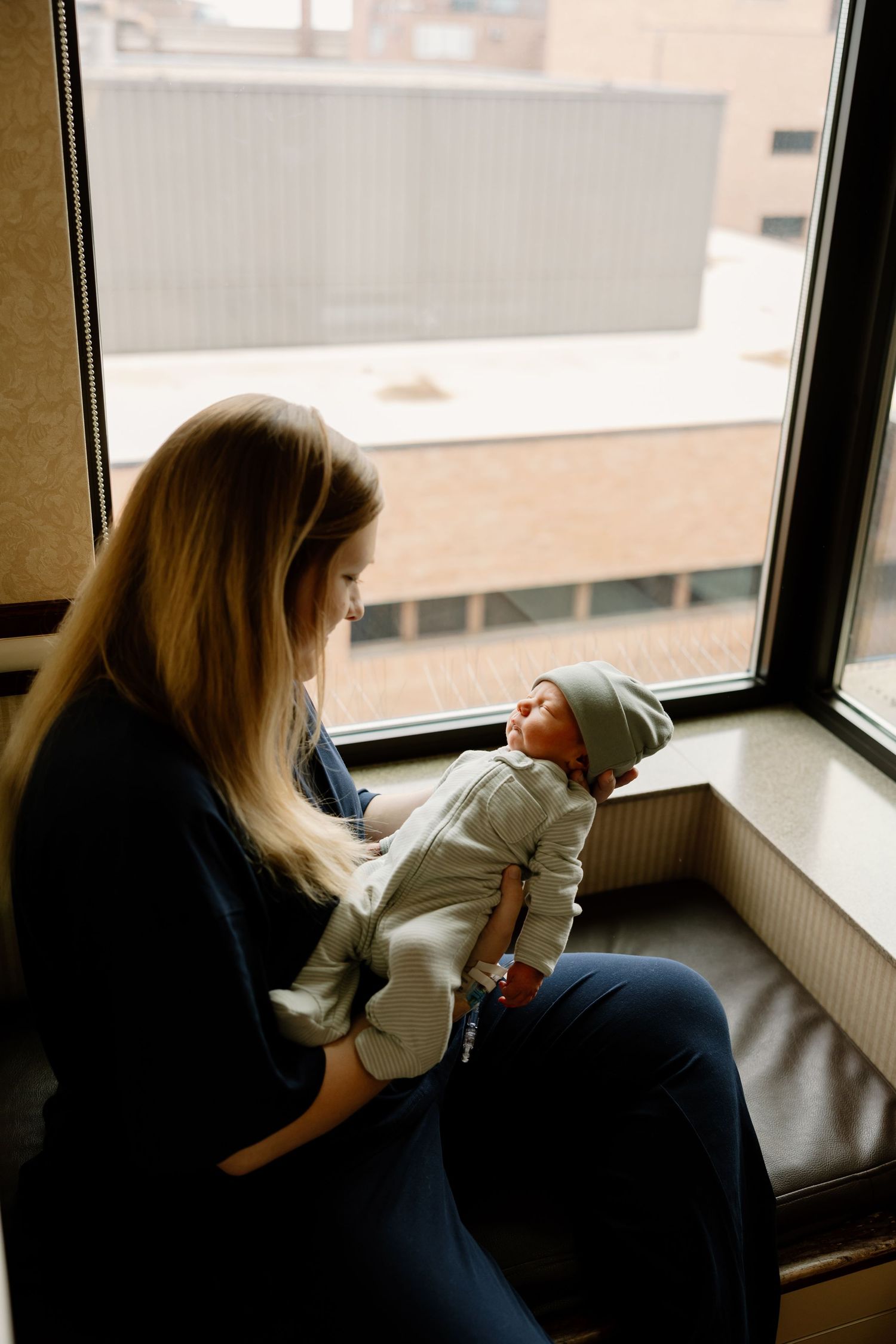 An intimate moment shows a parent cradling a newborn baby while sitting near a large window.