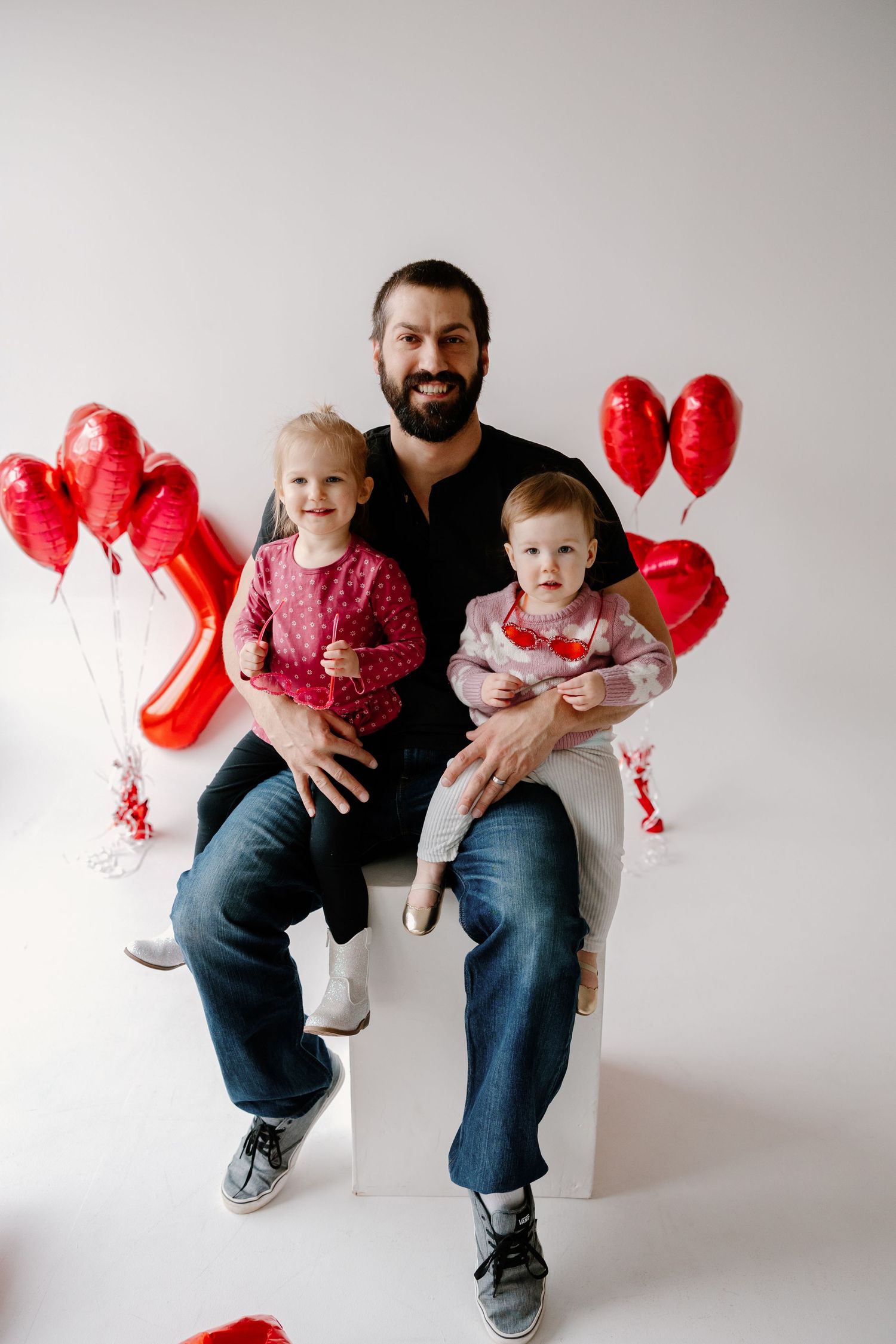 A joyful family photo session with red heart balloons against a white background for Valentine's Day.