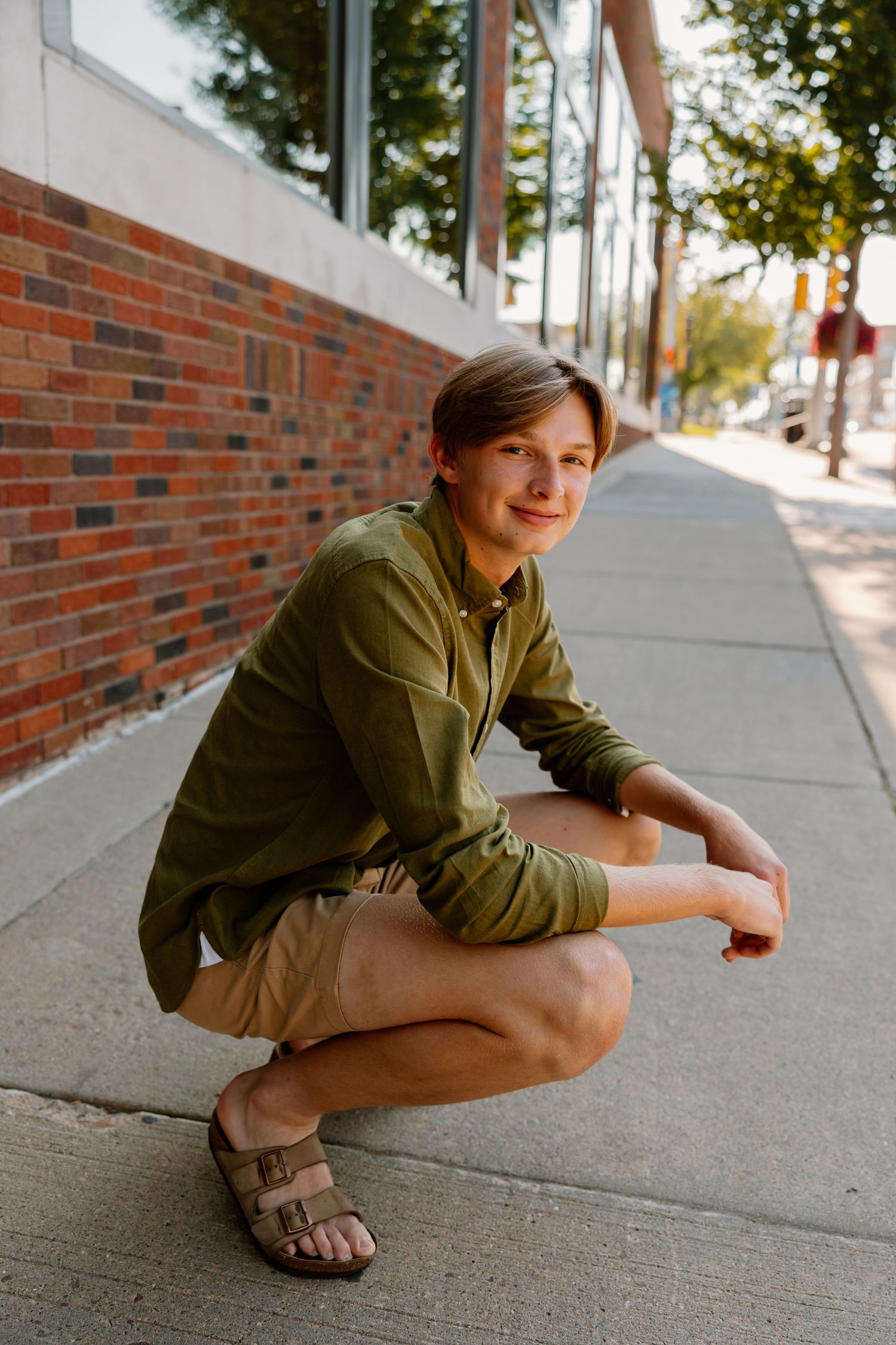 Someone wearing an olive green shirt crouches on a concrete sidewalk next to a brick wall in multiple similar poses.