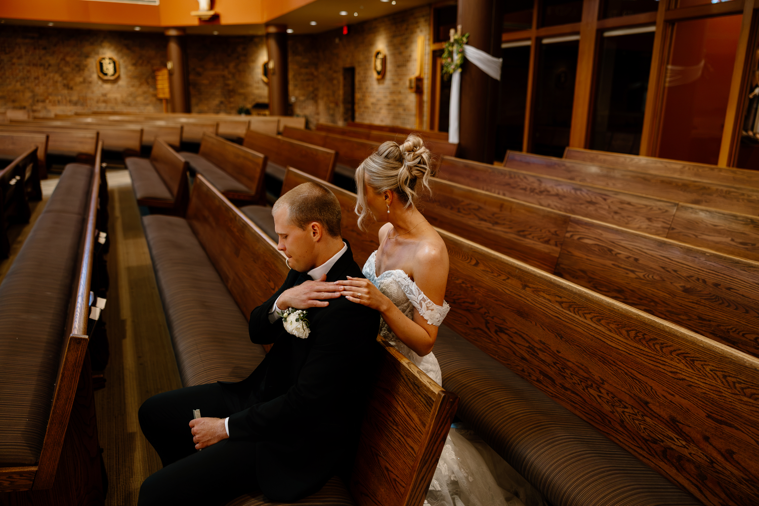 Bride and groom share an intimate moment sitting together in wooden church pews during their wedding ceremony.