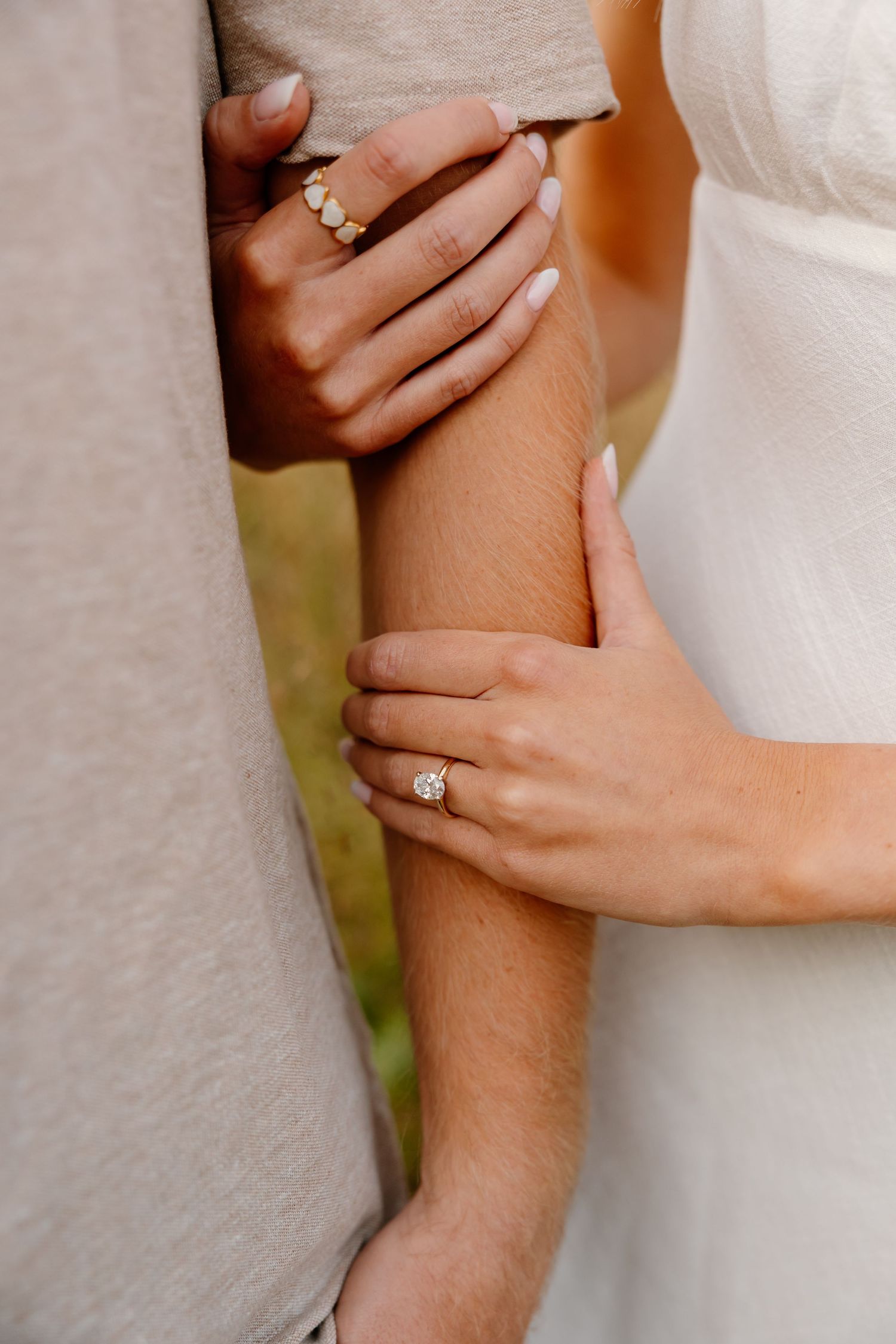 Wedding rings and engagement rings sparkle on clasped hands wearing white lacy fabric in a romantic pose.