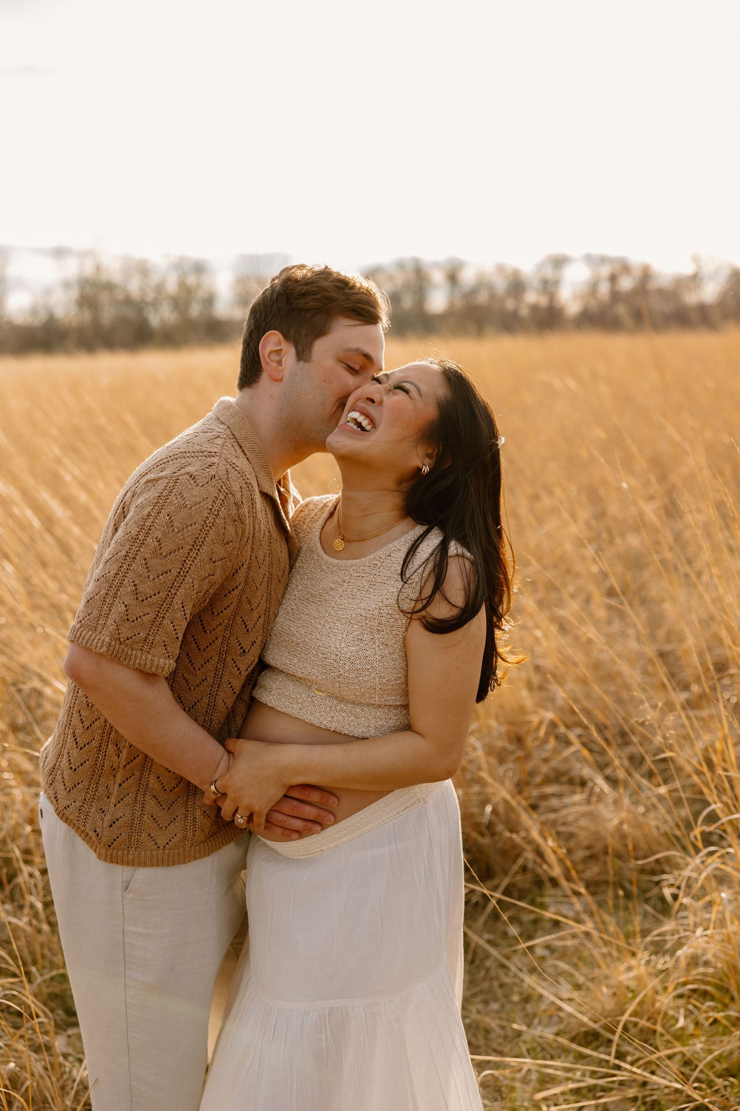 A couple shares an intimate moment in a golden wheat field during sunset.