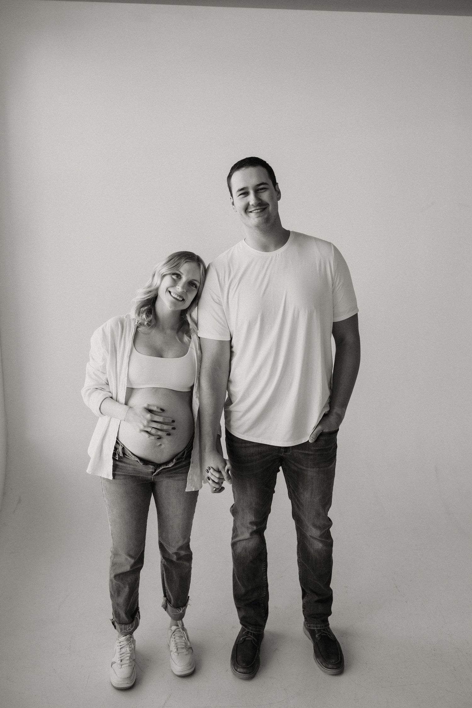 Black and white artistic photo showing legs and feet of two people standing side by side against a white wall. Riley Ro Photo Sioux Falls