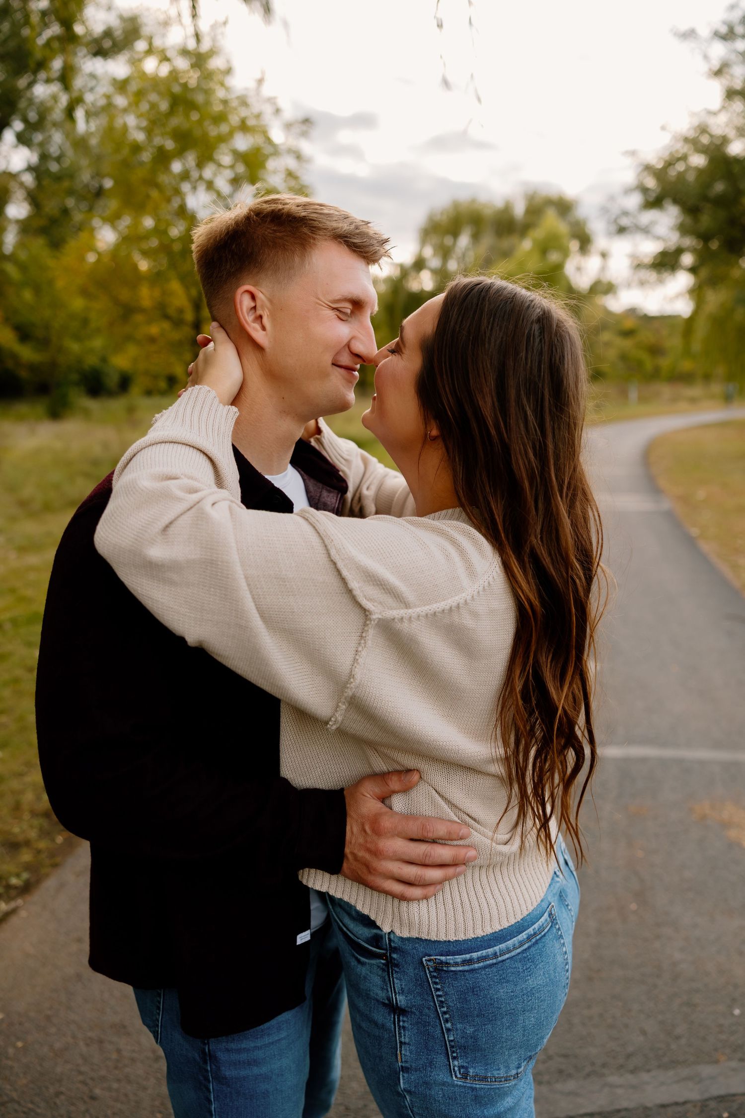 A romantic couple embraces on a winding park path during golden hour with autumn trees in the background. Riley Ro Photo Sioux Falls, SD