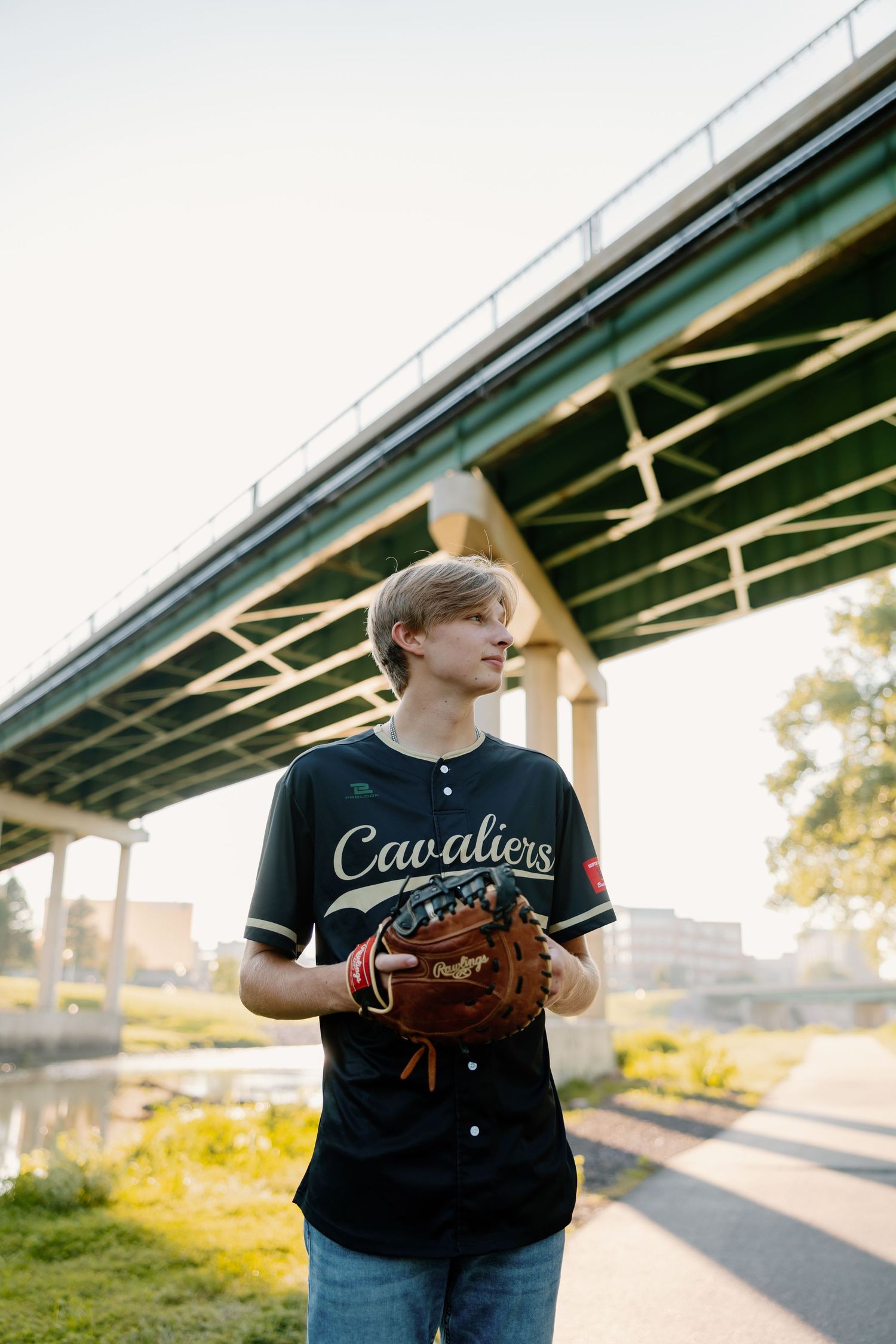 Baseball player in Cavaliers uniform poses with glove under bridge at sunset.