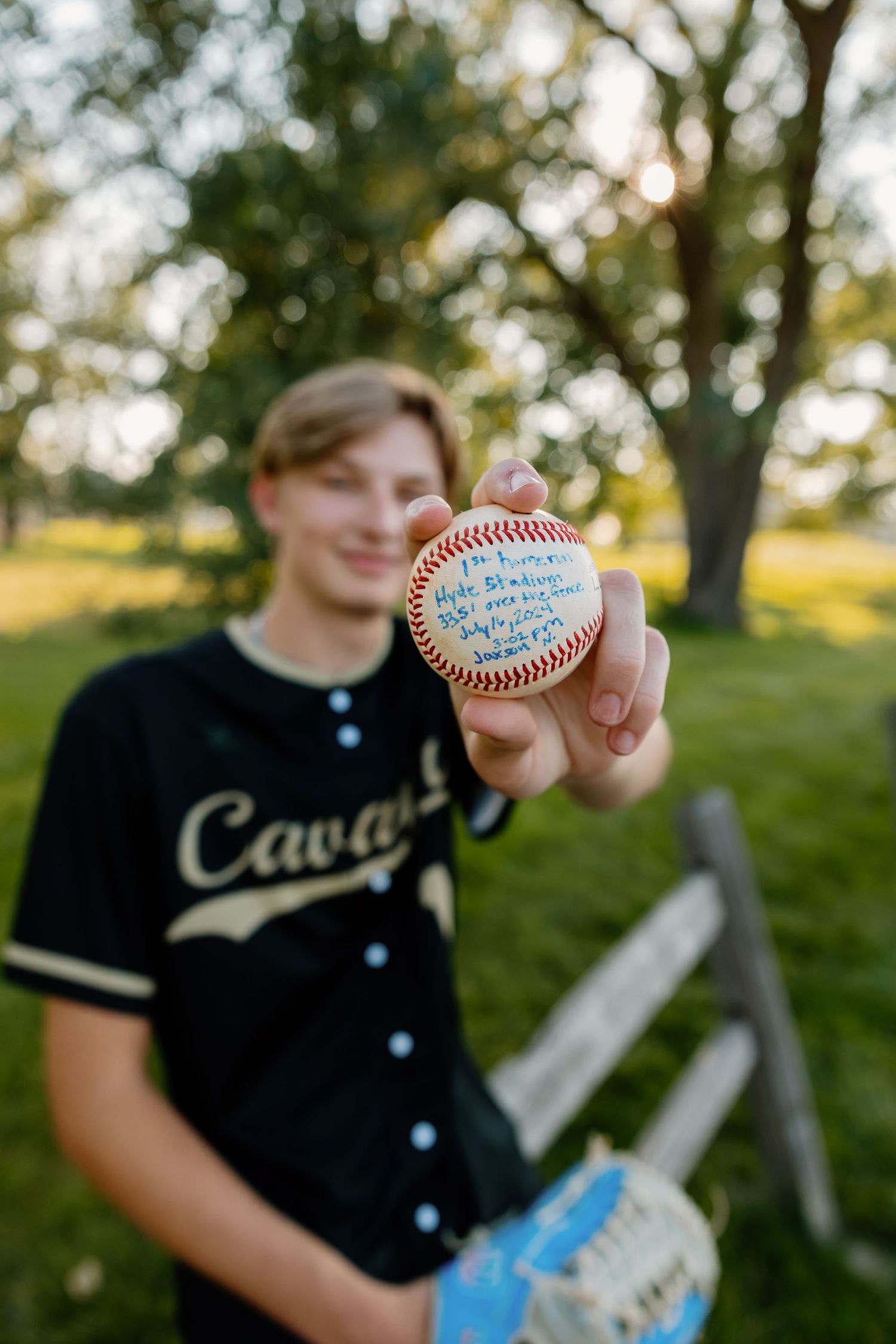 Baseball player in black Cubs jersey holds up autographed baseball during sunset photo session.