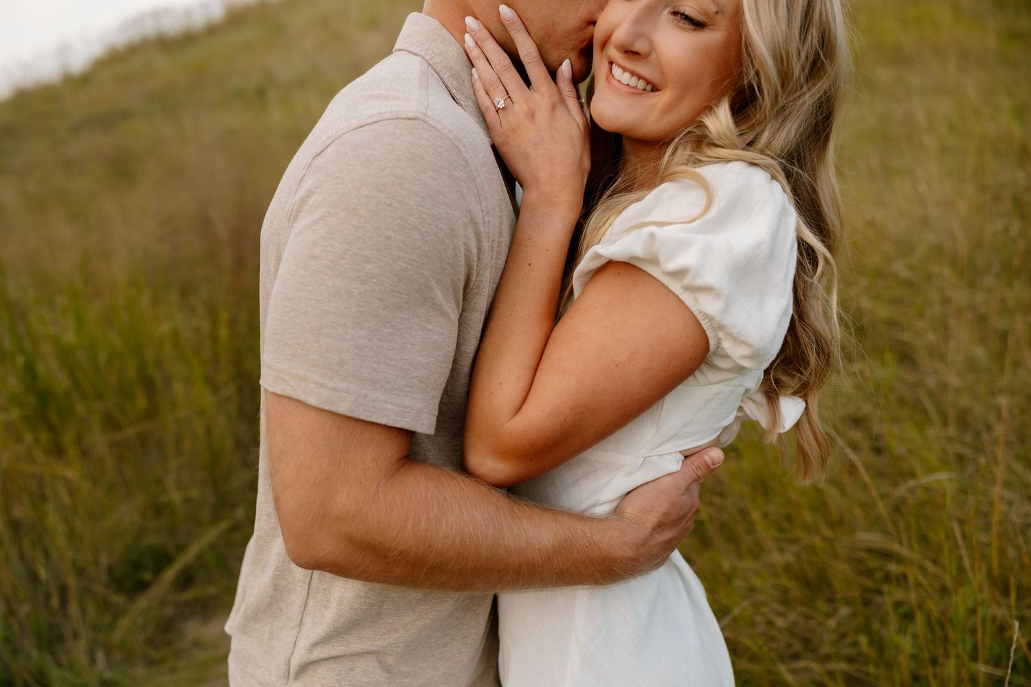 A romantic couple shares an intimate moment while embracing in a grassy meadow at sunset.
