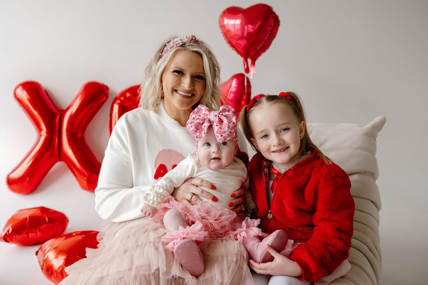 A Valentine's holiday portrait with red heart balloons, pink tulle dress, and white and red attire against gray backdrop.