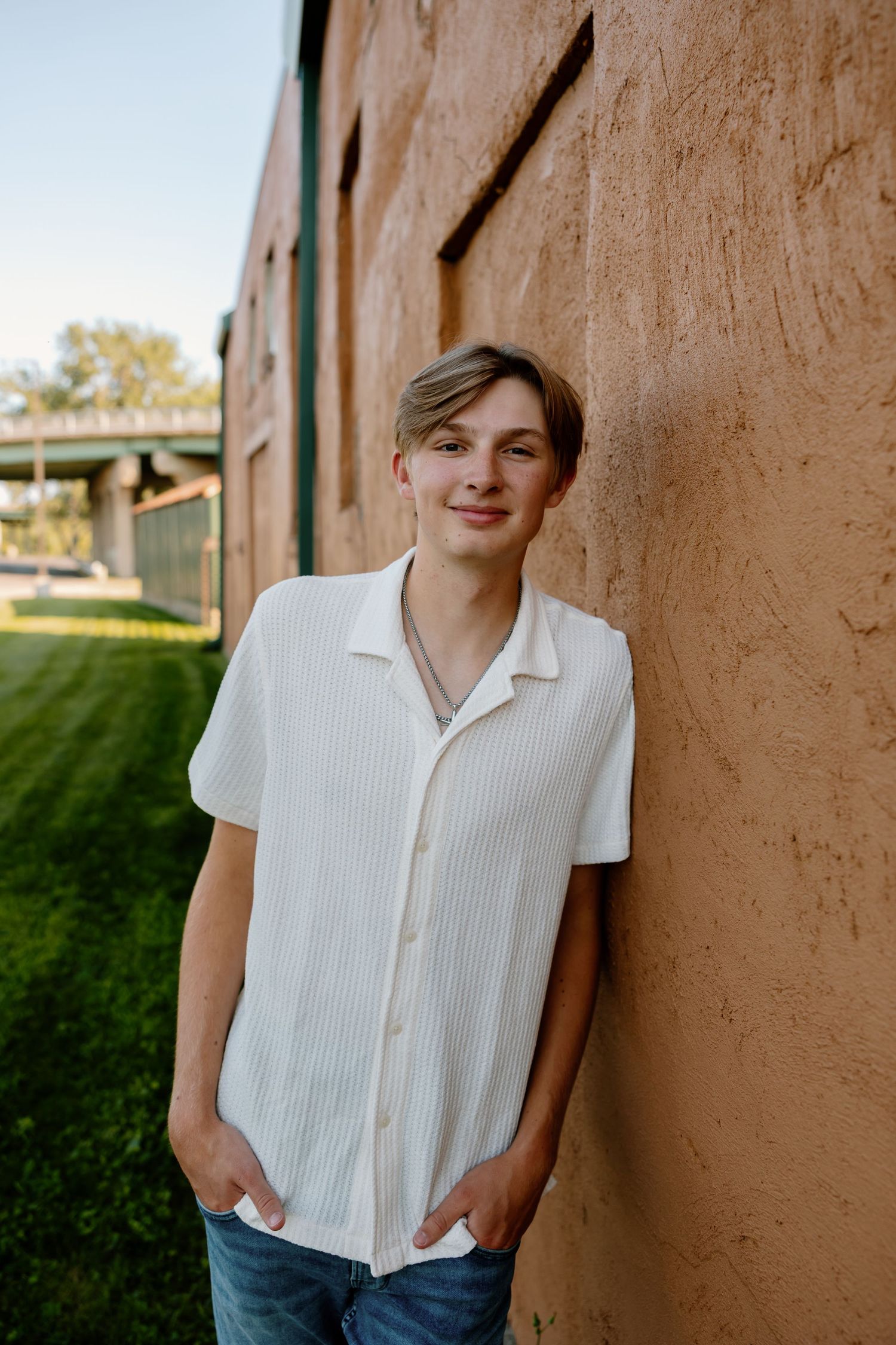 Person in white button-up shirt posing against terracotta wall in natural lighting.