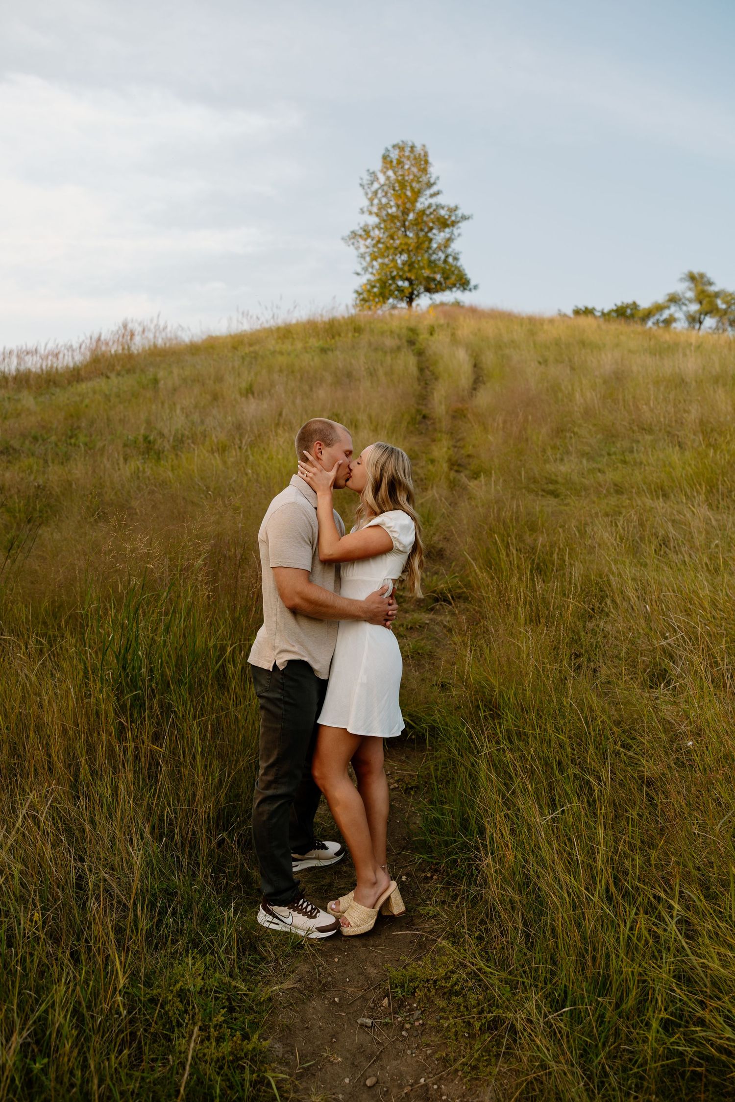 A romantic couple embracing in tall grass on a hillside during golden hour.