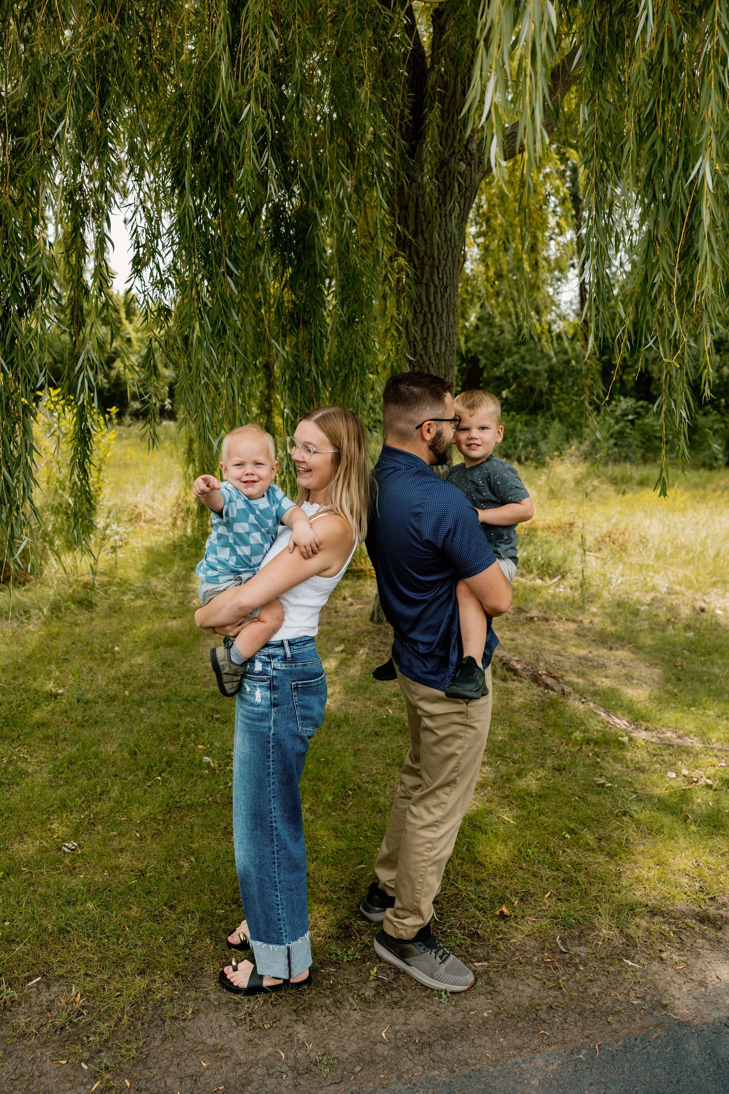 Family stands together under a cascading willow tree on a sunny summer day.