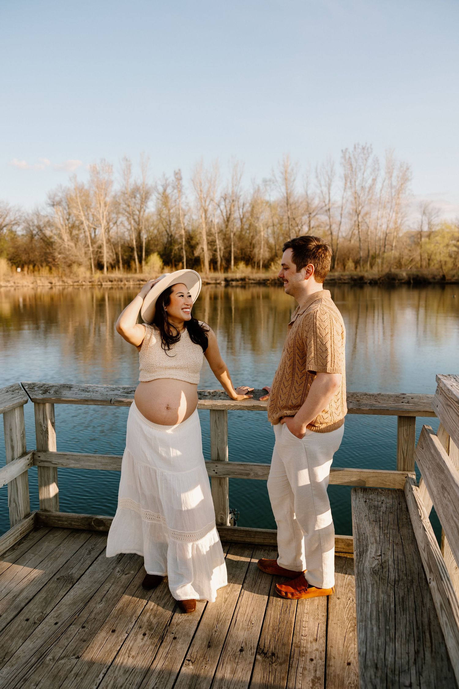 A maternity photoshoot on a wooden dock shows a couple sharing a tender moment by the lake.