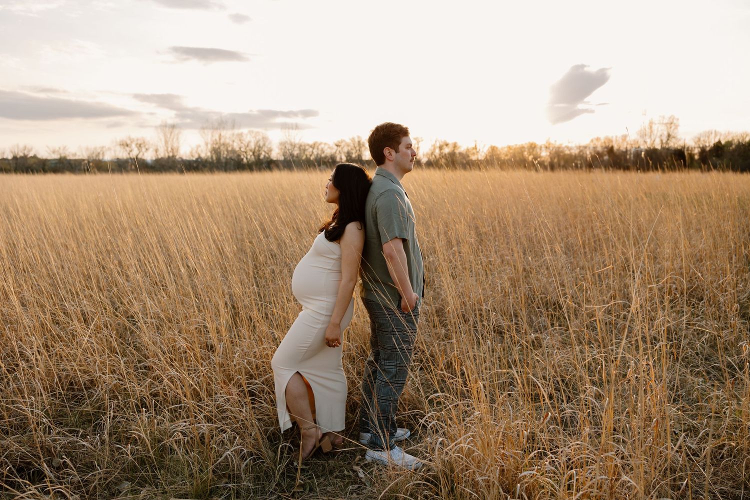 Two people stand back-to-back in a golden wheat field at sunset creating a romantic silhouette effect.