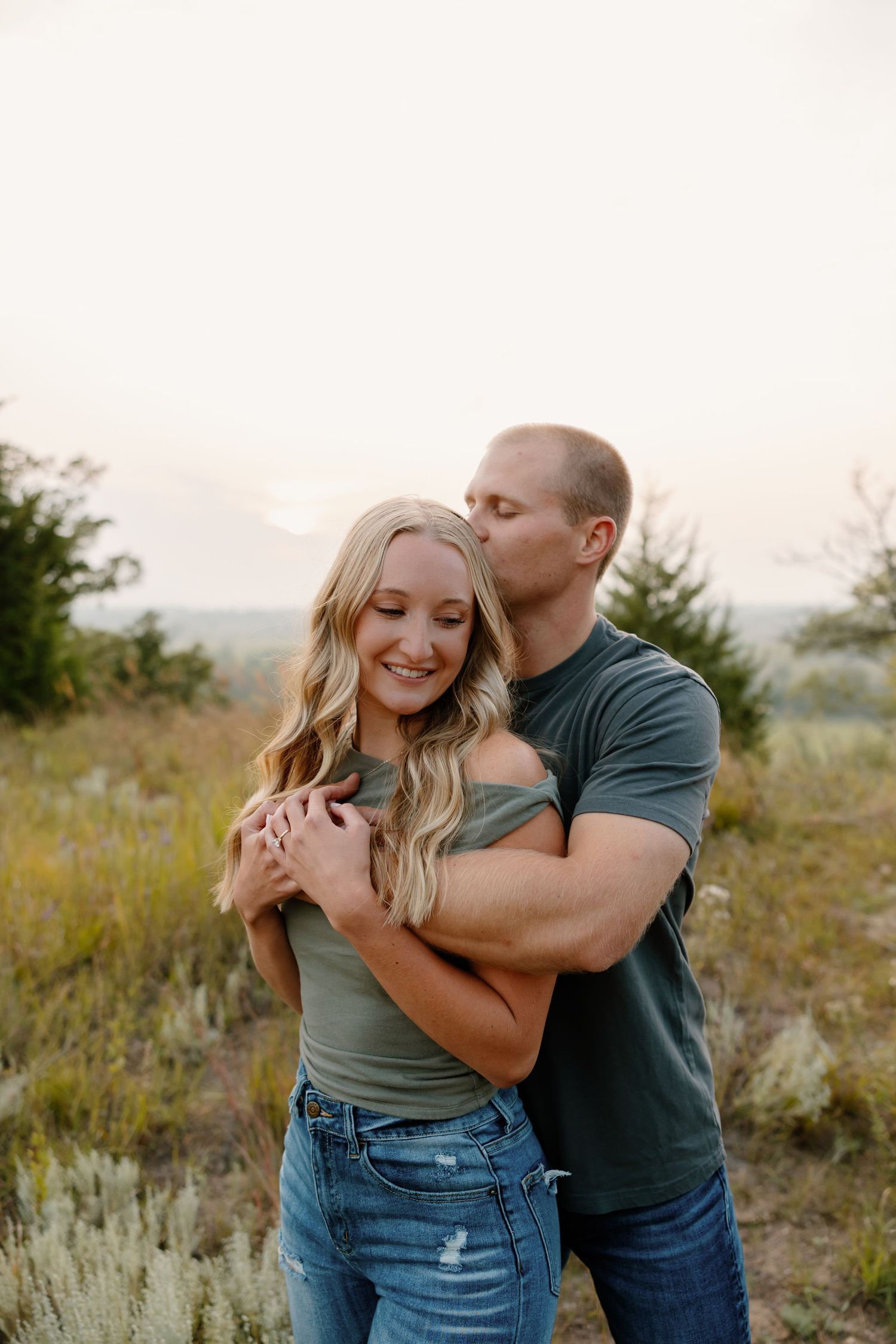 Romantic couple embracing in field during sunset with mountains in background. sioux falls photographer riley ro photo